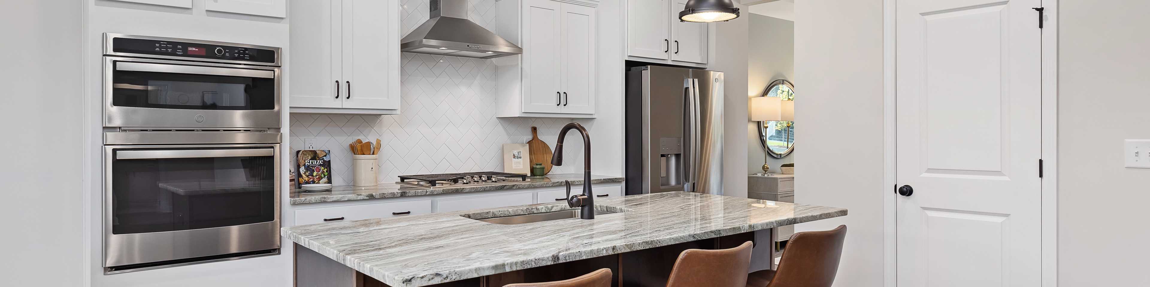 Spacious modern kitchen at Woodland Crossing in Zebulon NC with white shaker cabinets, quartz island, leather bar stools, stainless appliances