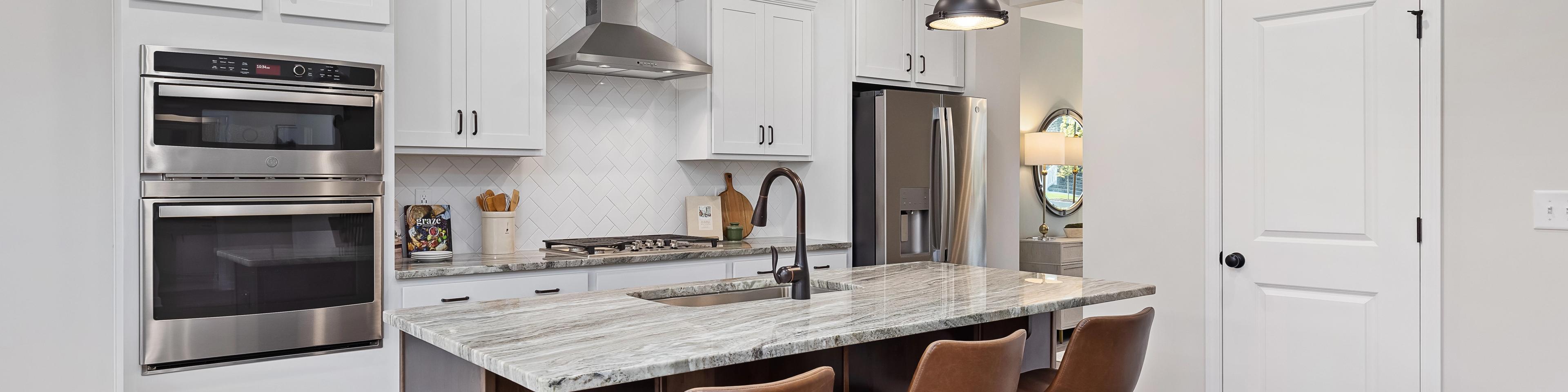 Spacious modern kitchen at Woodland Crossing in Zebulon NC with white shaker cabinets, quartz island, leather bar stools, stainless appliances