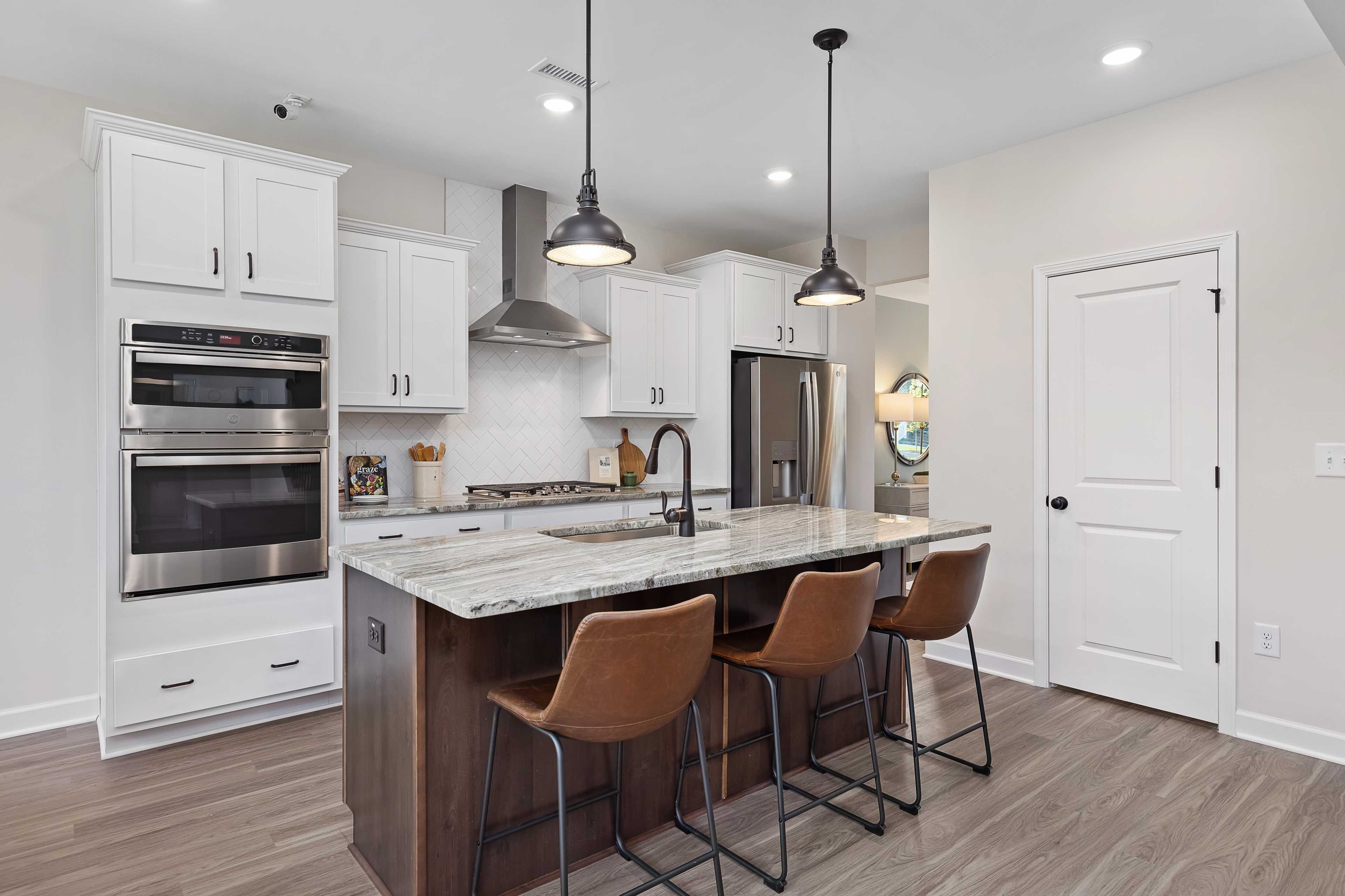 Spacious modern kitchen at Woodland Crossing in Zebulon NC with white shaker cabinets, granite island, leather bar stools, and pendant lights
