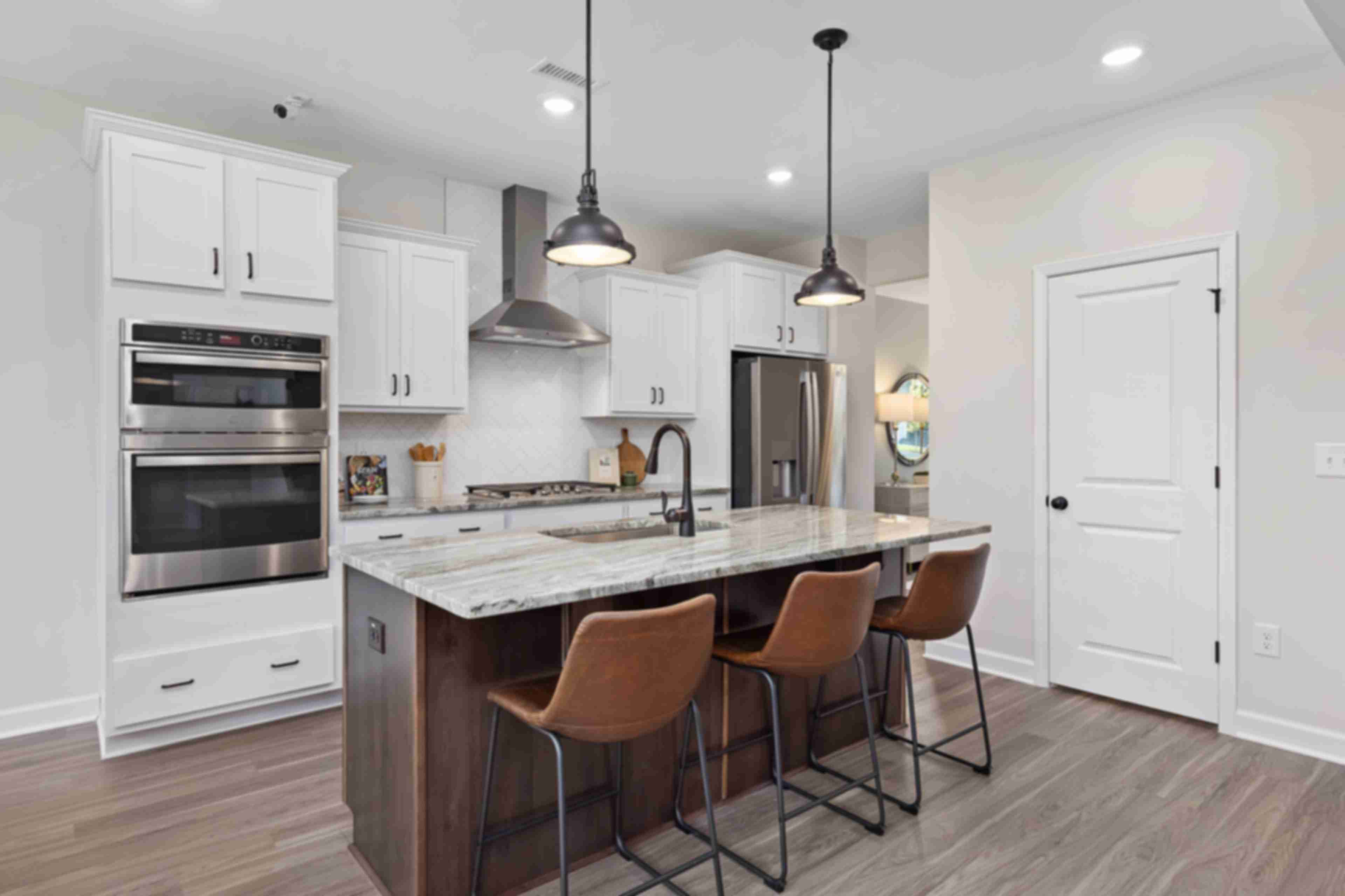 Spacious modern kitchen at Woodland Crossing in Zebulon NC with white shaker cabinets, quartz island, leather bar stools, stainless appliances