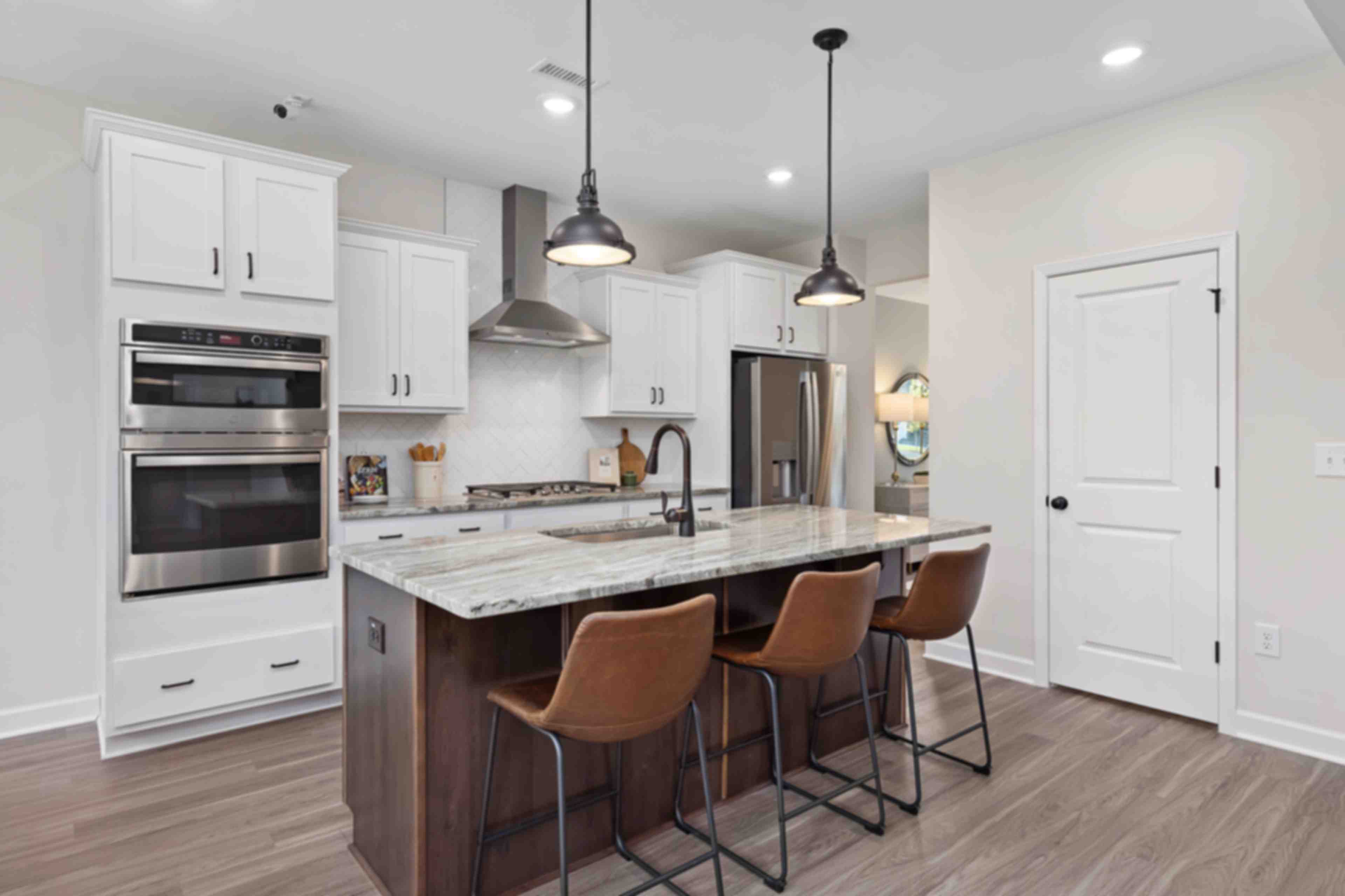 Spacious kitchen at Rockport in Wake Forest NC by Davidson Homes featuring white cabinets, quartz island with leather stools, and pendant lights
