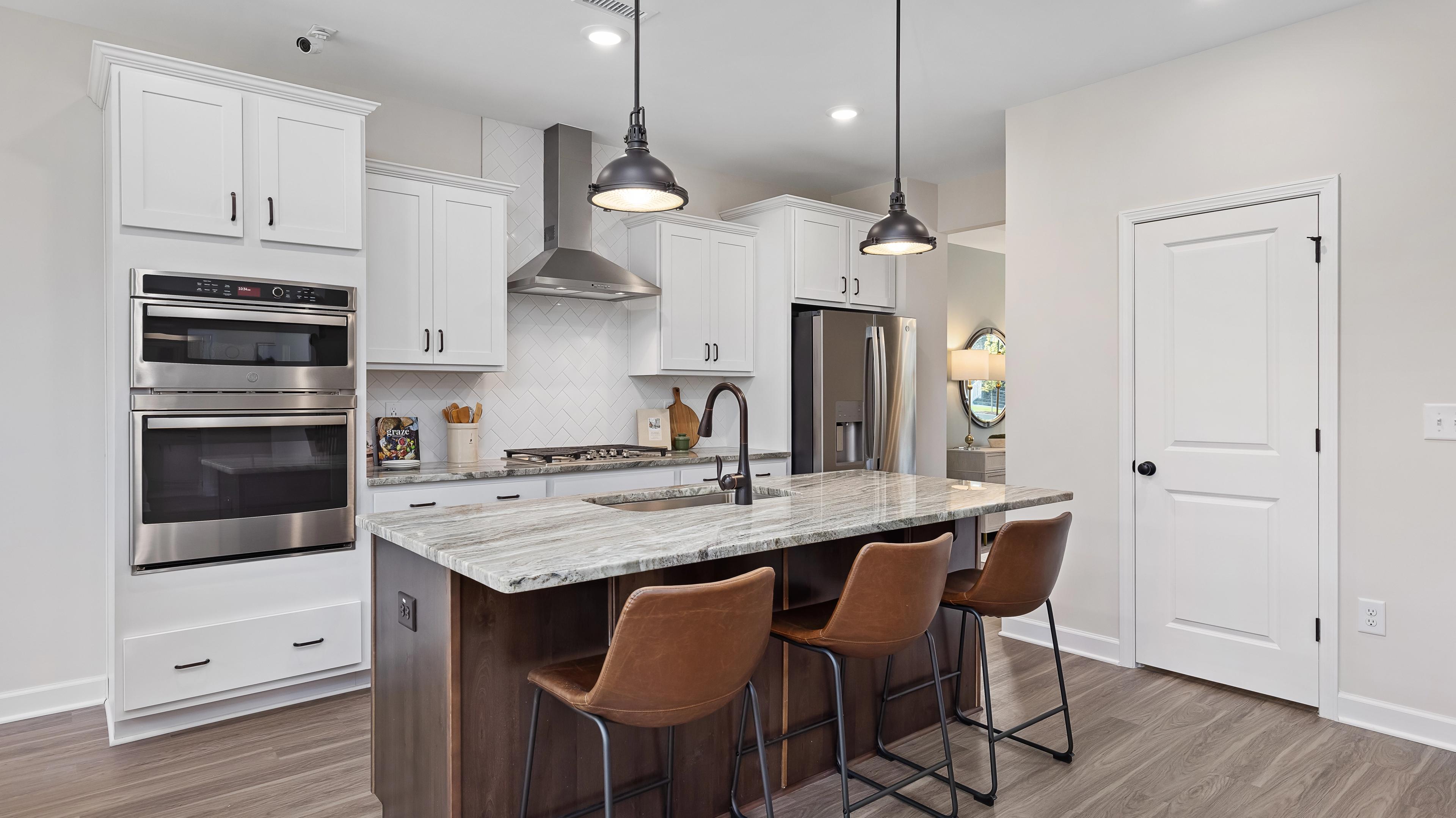 Spacious modern kitchen at Woodland Crossing in Zebulon NC with white shaker cabinets, quartz island, leather bar stools, stainless appliances