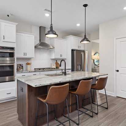 Spacious modern kitchen at Woodland Crossing in Zebulon NC with white shaker cabinets, quartz island, leather bar stools, stainless appliances