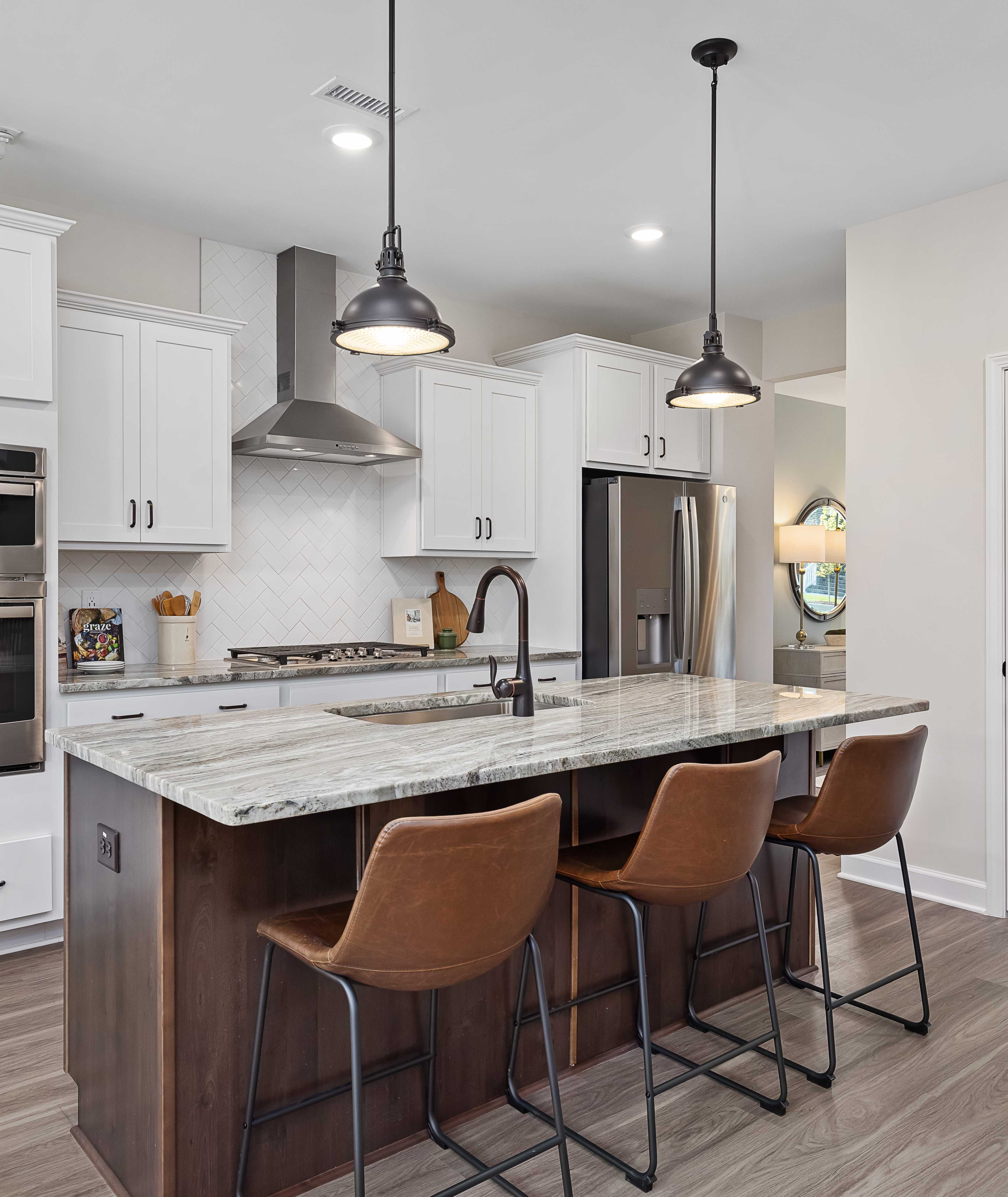 Spacious modern kitchen at Woodland Crossing in Zebulon NC with white shaker cabinets, quartz island, leather bar stools, stainless appliances