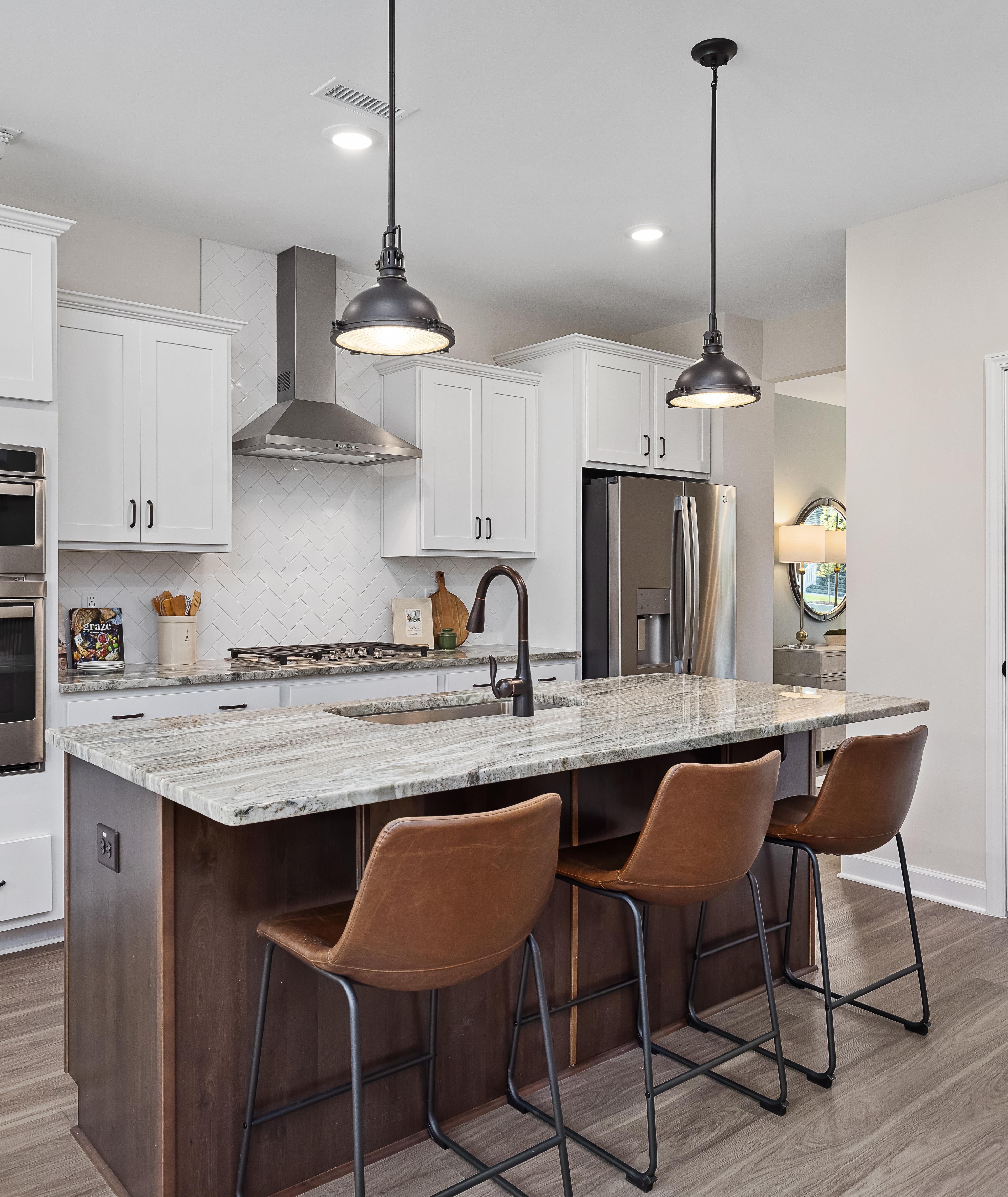 Spacious modern kitchen at Woodland Crossing in Zebulon NC with white shaker cabinets, quartz island, leather bar stools, stainless appliances