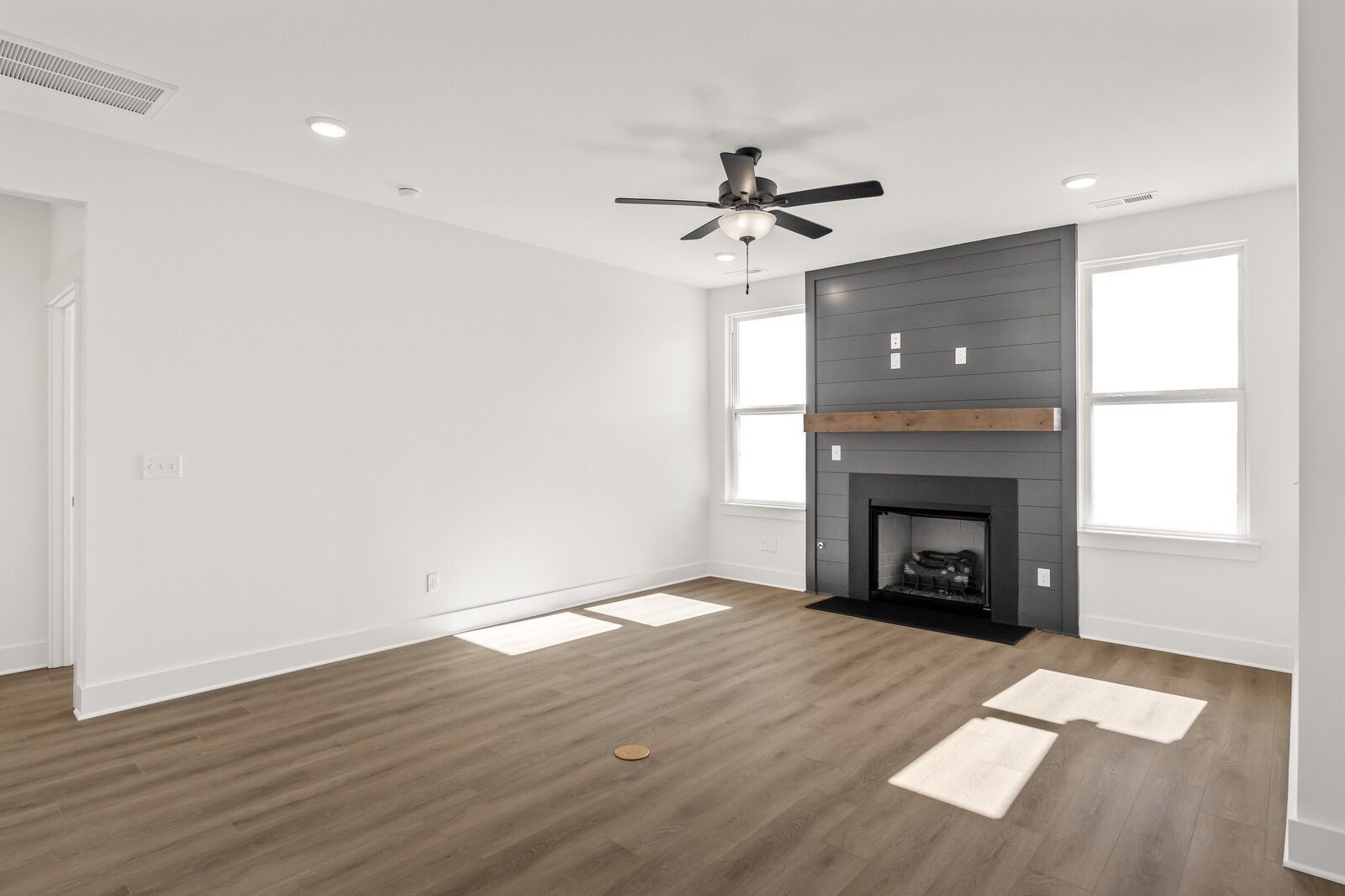 Modern living room with gas fireplace, wood mantel, ceiling fan, large windows, and hardwood floors in Davidson Homes The Ash A, Gallatin, TN