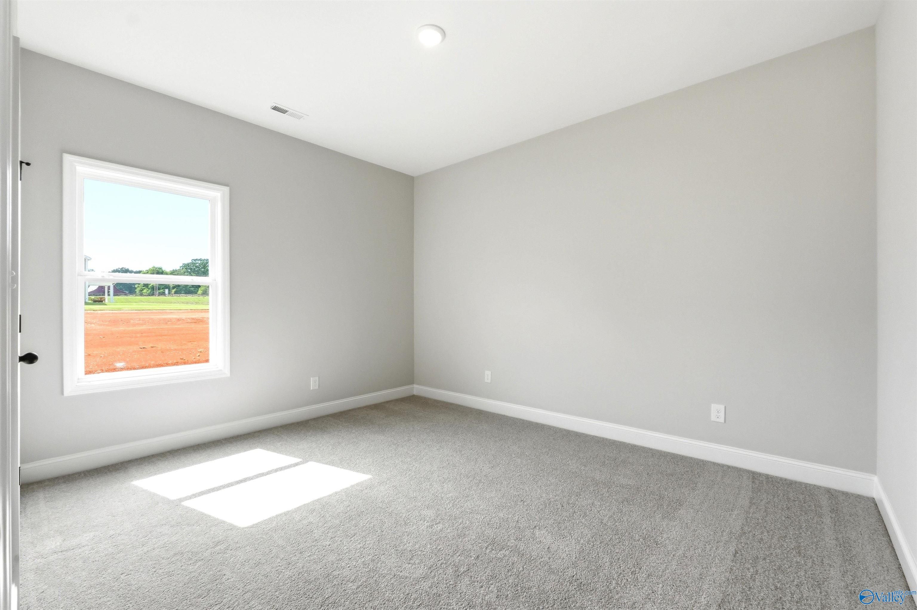 Bright bedroom with neutral carpet and walls in The Daphne F floor plan at Berry Cove, New Market, Alabama.