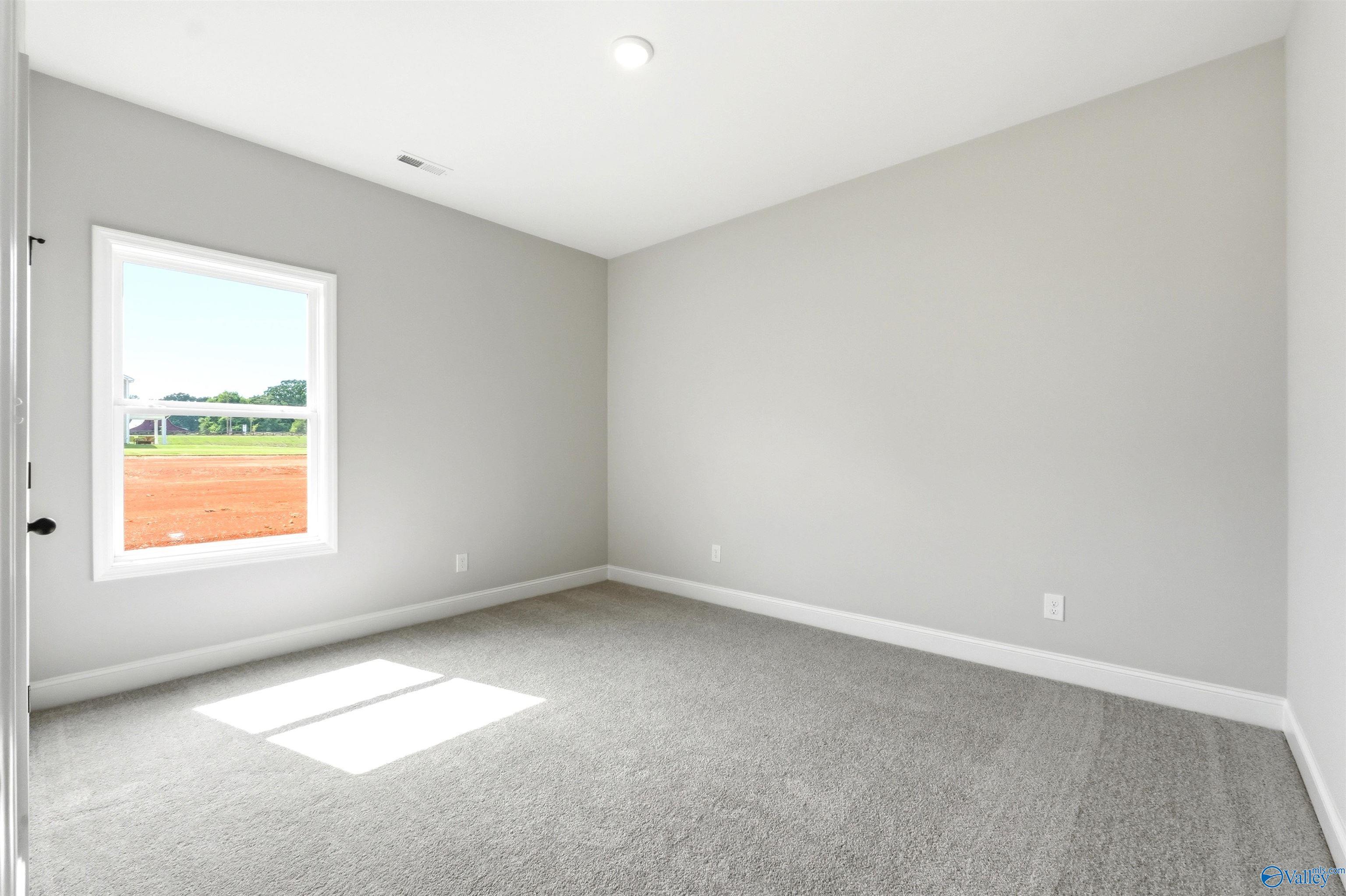 Bright bedroom with neutral carpet and walls in The Daphne F floor plan at Berry Cove, New Market, Alabama.