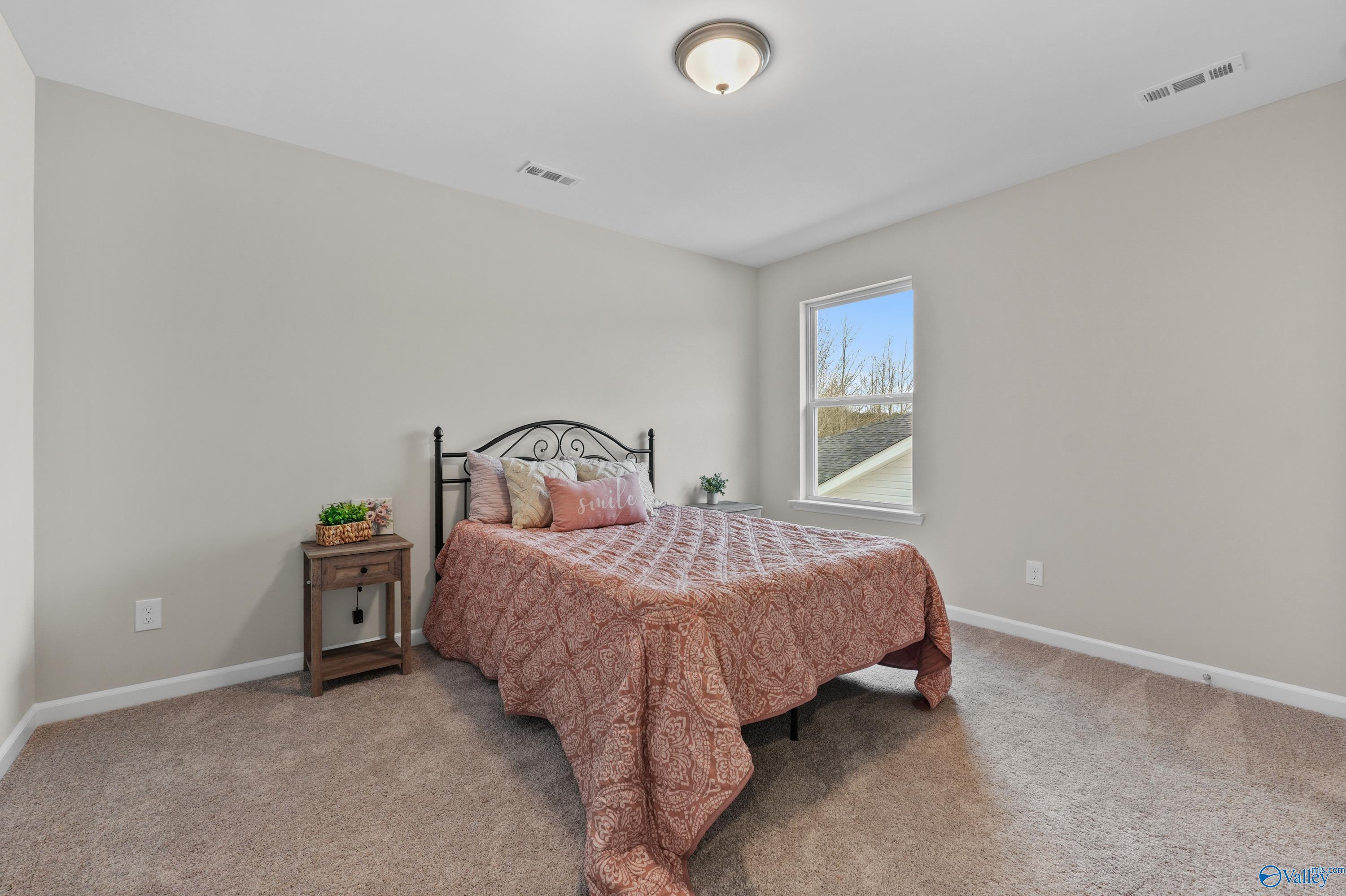 Cozy bedroom with queen bed, wrought iron headboard, neutral walls in Davidson Homes The Stella, Hazel Green, Alabama