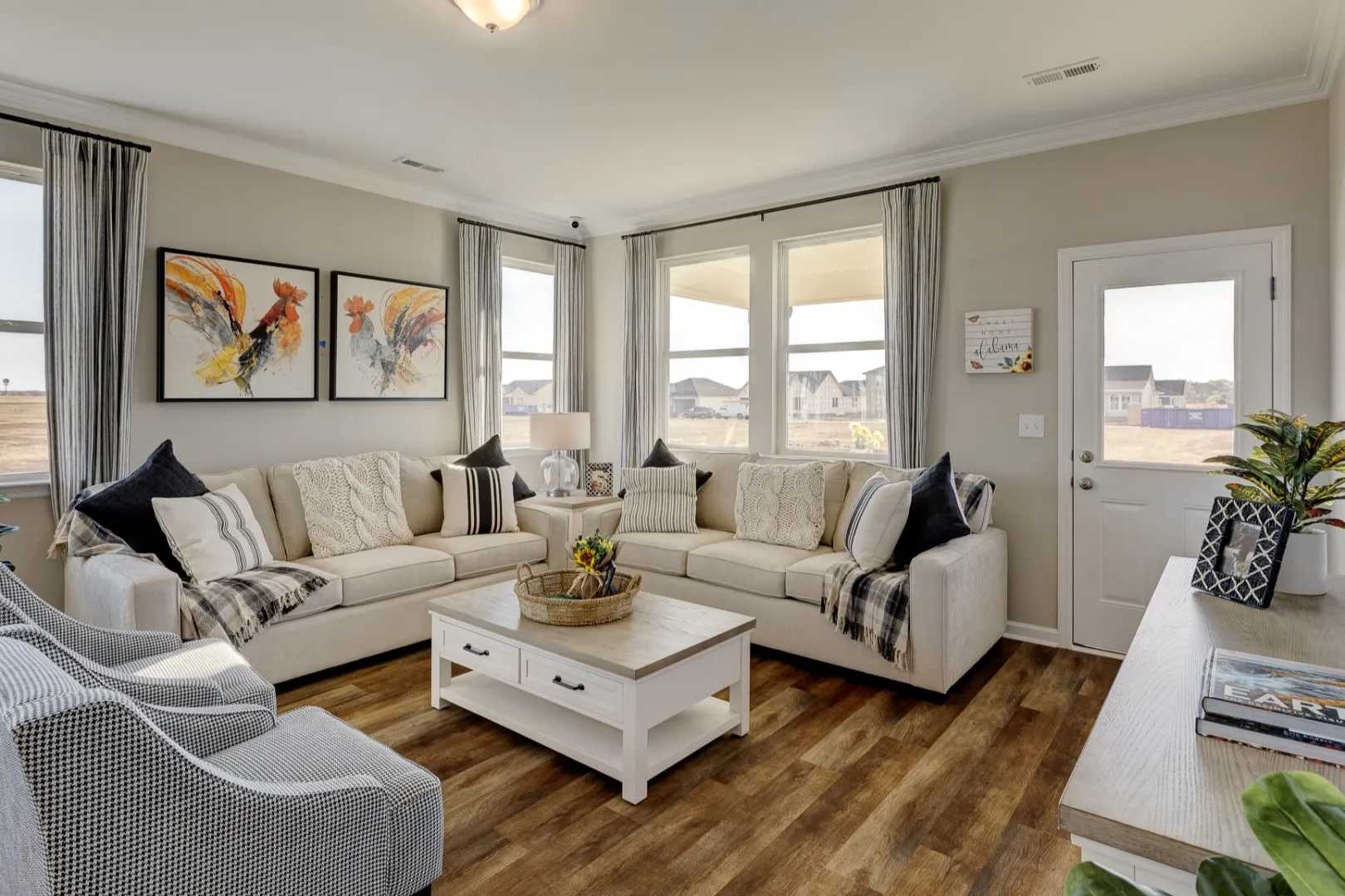 Spacious living room in The Aurora B by Davidson Homes featuring beige L-shaped sofa, abstract art, potted plants, and large windows