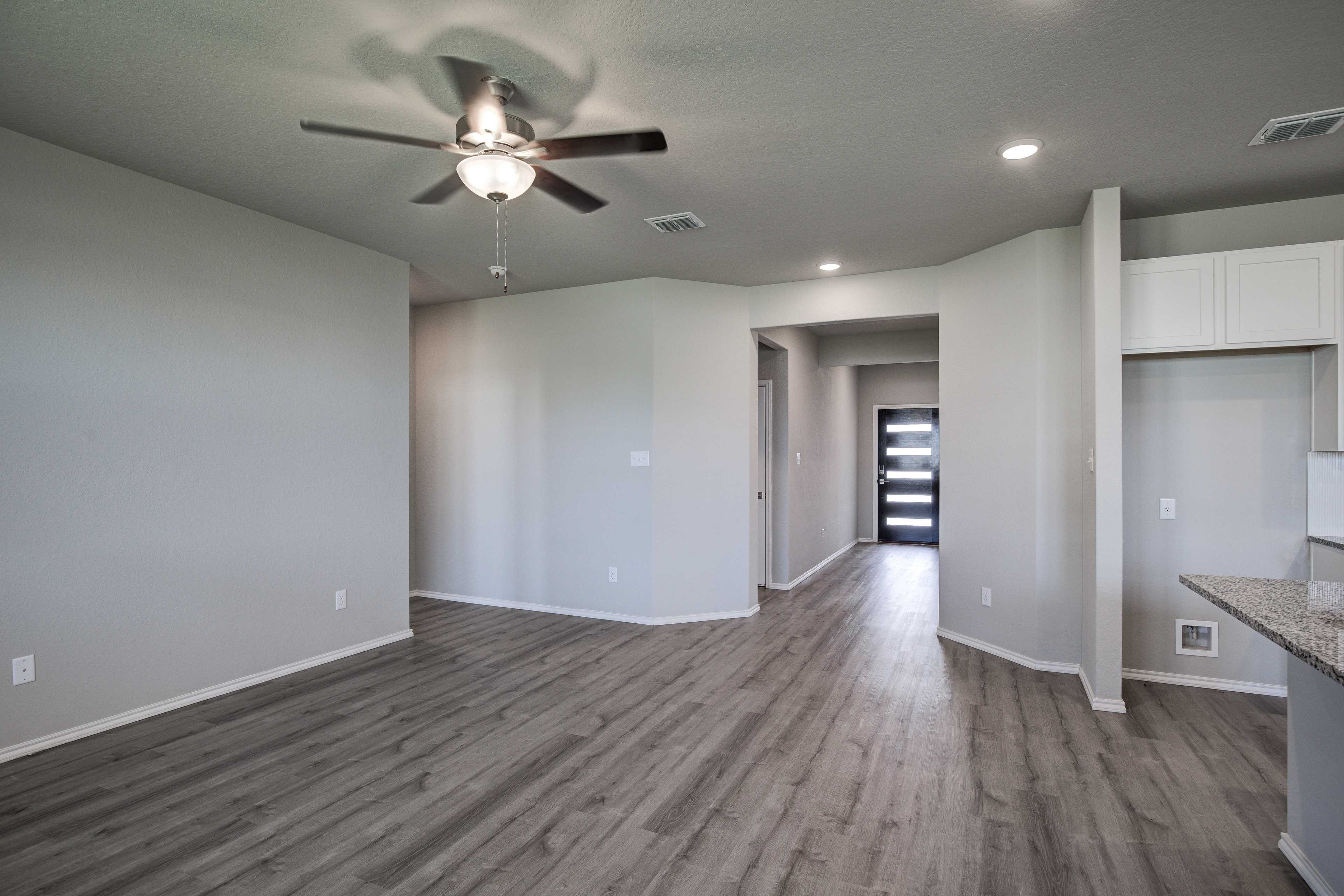 Spacious open-concept living area in The Asheville home design with ceiling fan, hardwood floors, gray walls, and entry hallway