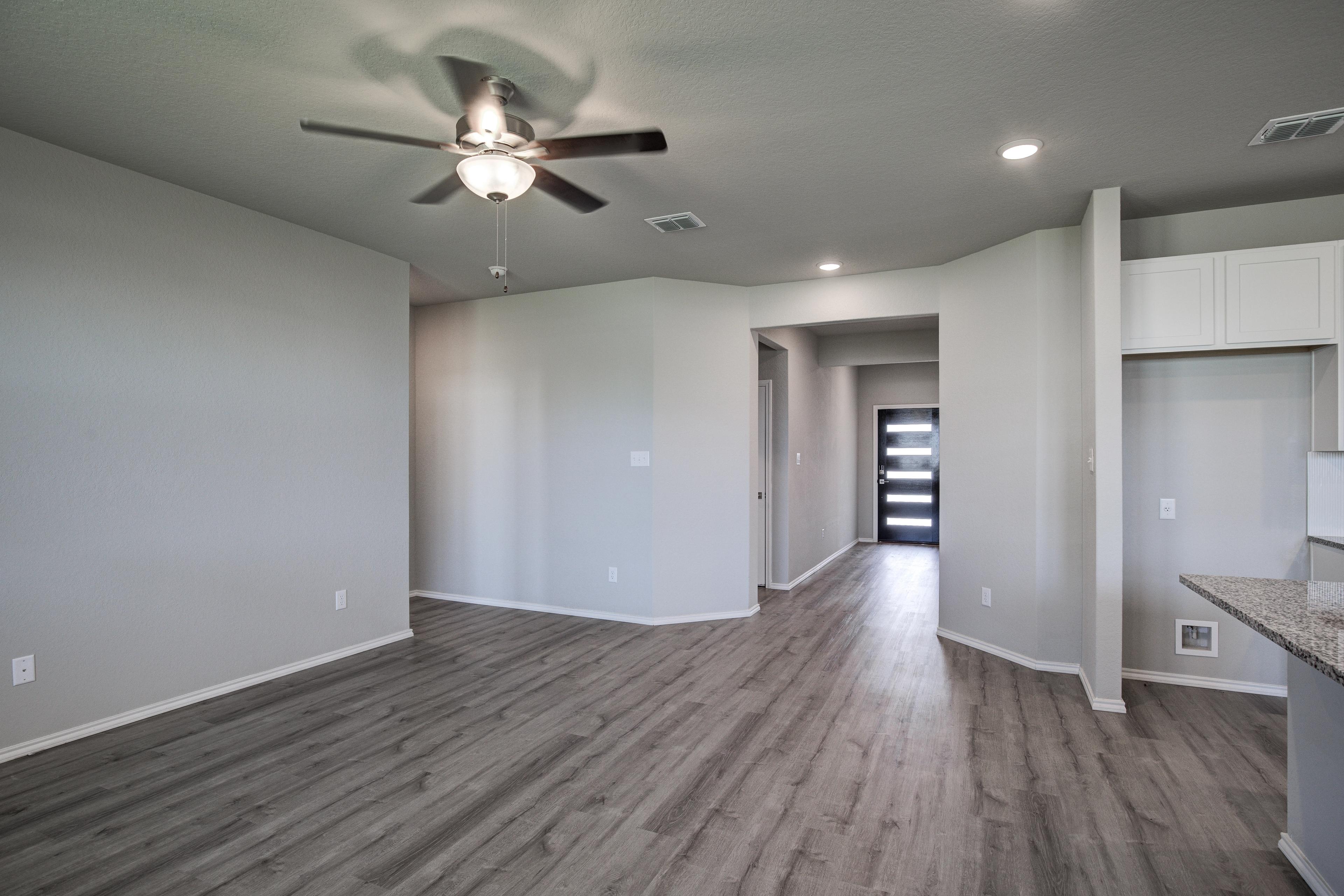 Spacious open-concept entry and living area in The Asheville home design featuring gray walls, wood laminate flooring, ceiling fan, and modern kitchen cabinets