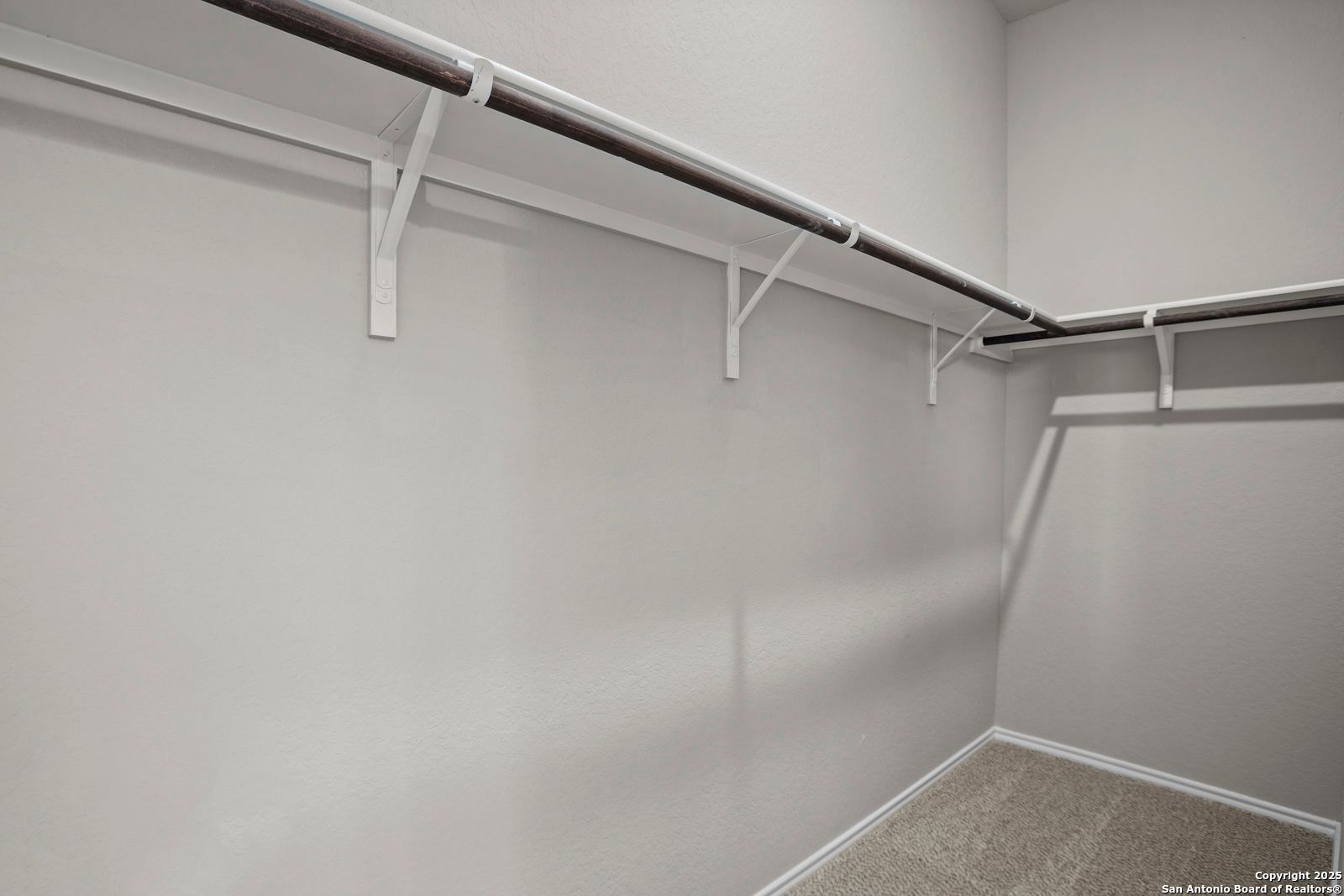 Spacious walk-in closet with white shelving brackets and hanging rods in neutral gray tones, The Collin B by Davidson Homes, Seguin Texas