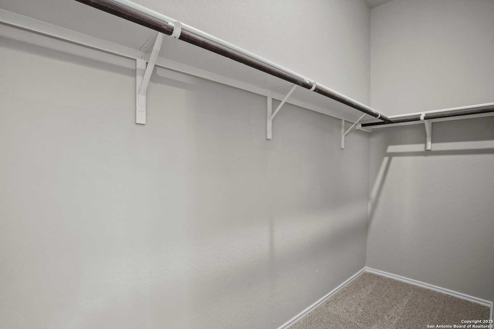 Spacious walk-in closet with white shelving brackets and hanging rods in neutral gray tones, The Collin B by Davidson Homes, Seguin Texas