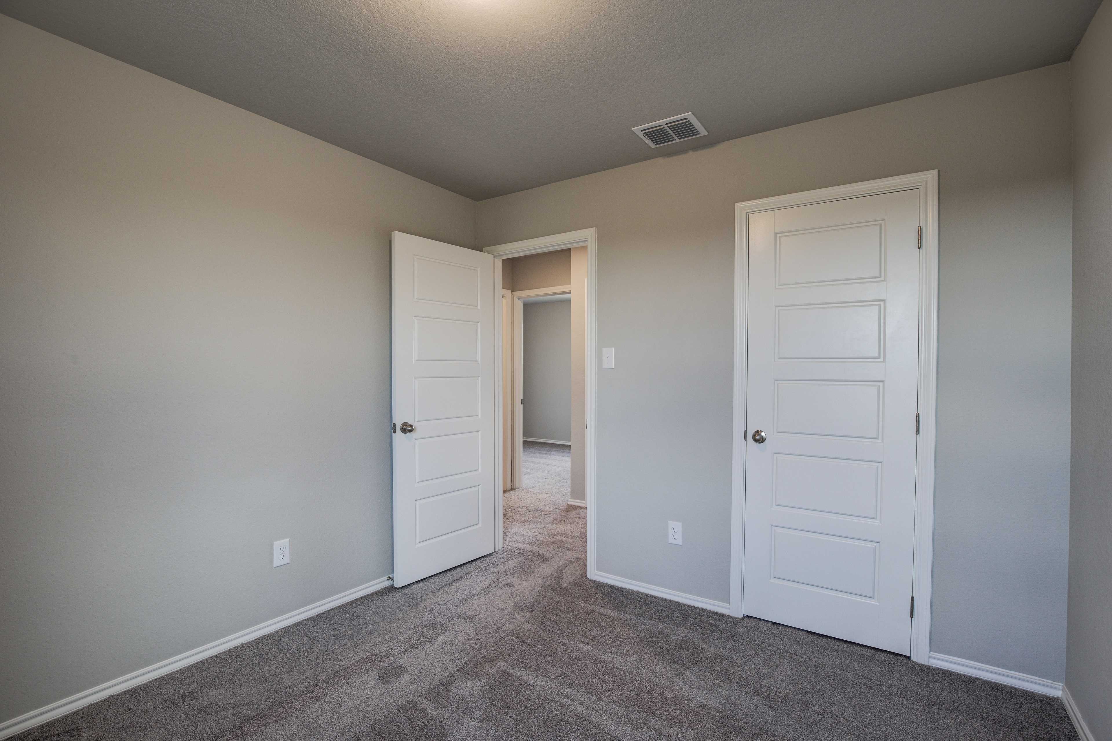 Spacious bedroom in The Blanco B with neutral beige walls, carpeted floor, open doors to hallway