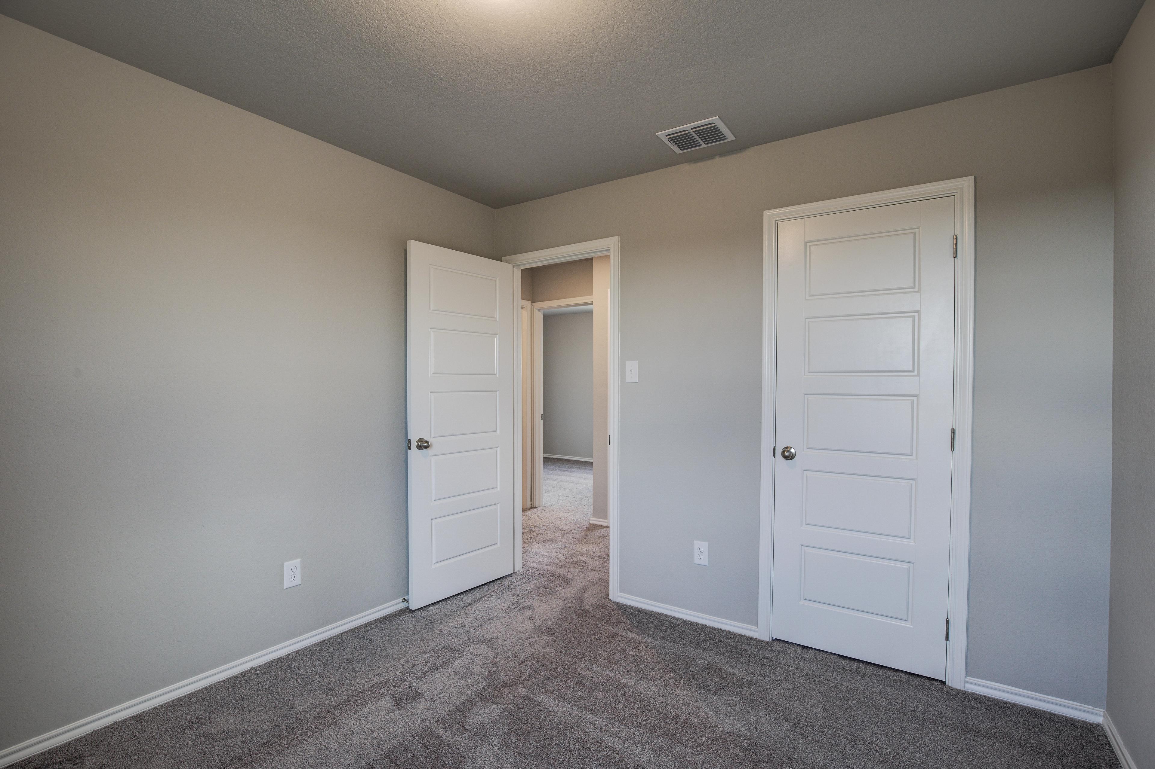 Spacious secondary bedroom in The Blanco C with beige walls, carpeted floor, double doors, and vaulted ceiling by Davidson Homes