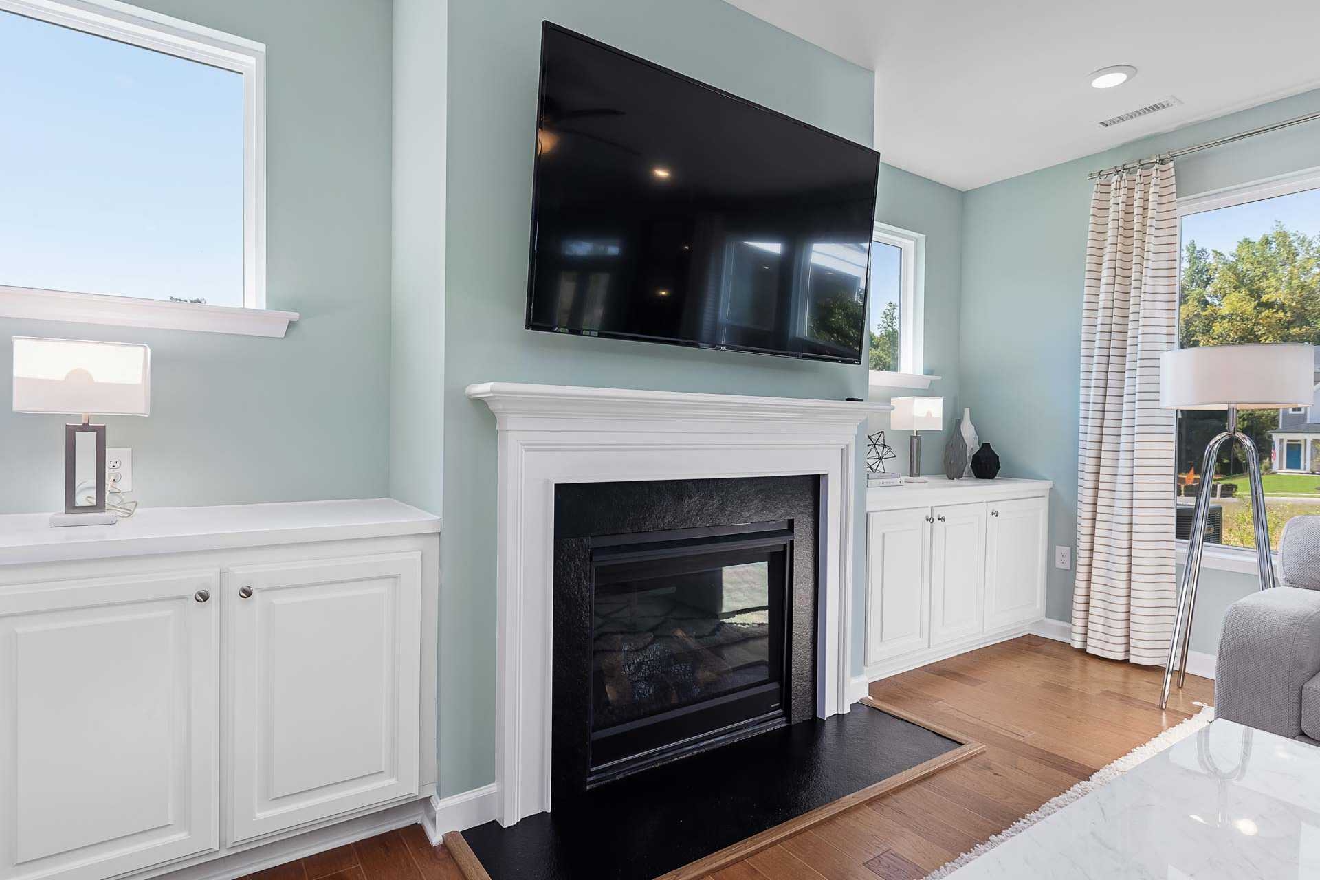 Cozy living room with white gas fireplace, mounted TV, built-in cabinets, blue walls and hardwood floors at Highland Forest in Fuquay-Varina, NC