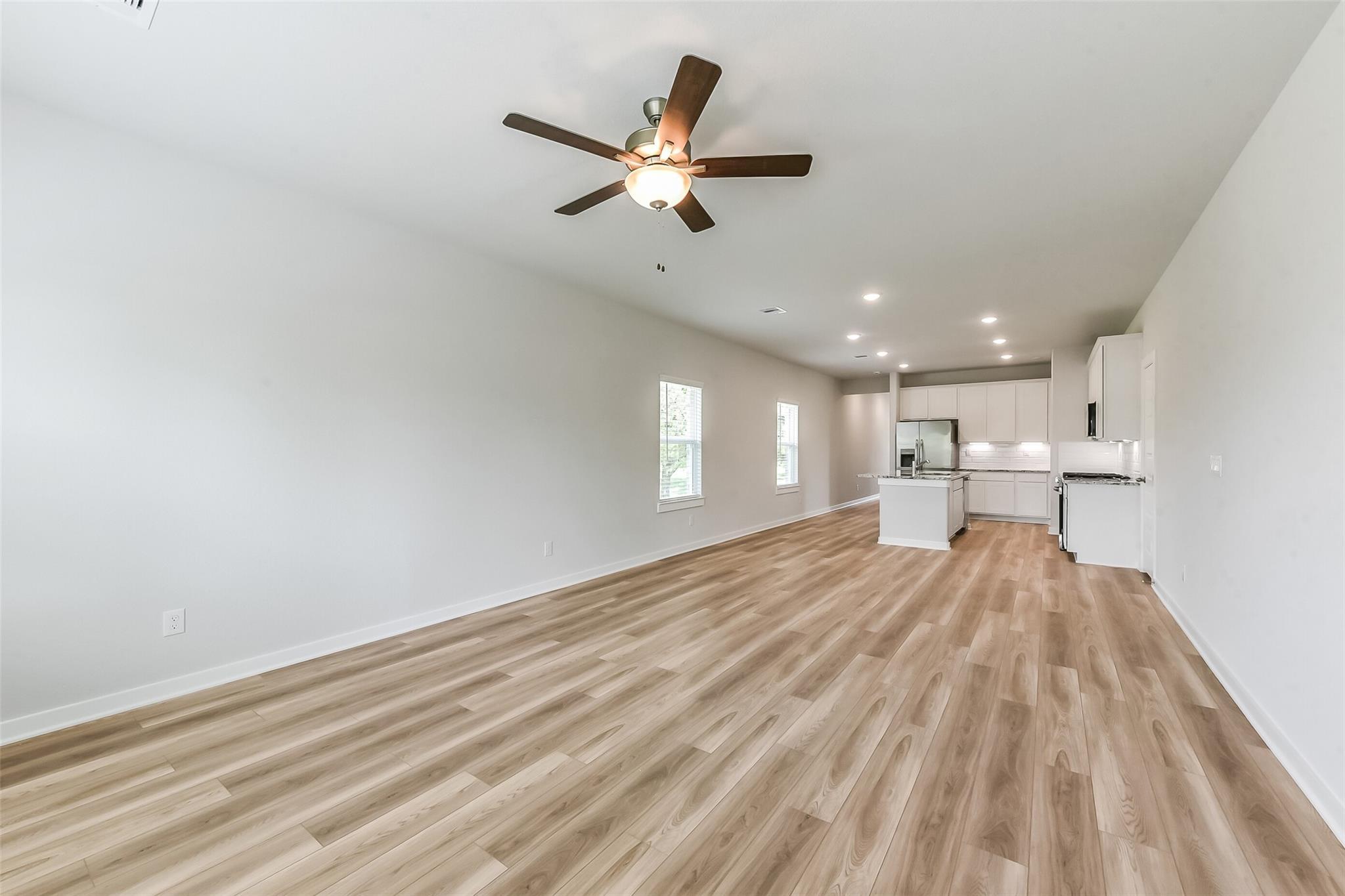 Open-concept living room with light wood floors, ceiling fan, and adjacent white kitchen in Davidson Homes The Frio G, Magnolia, Texas