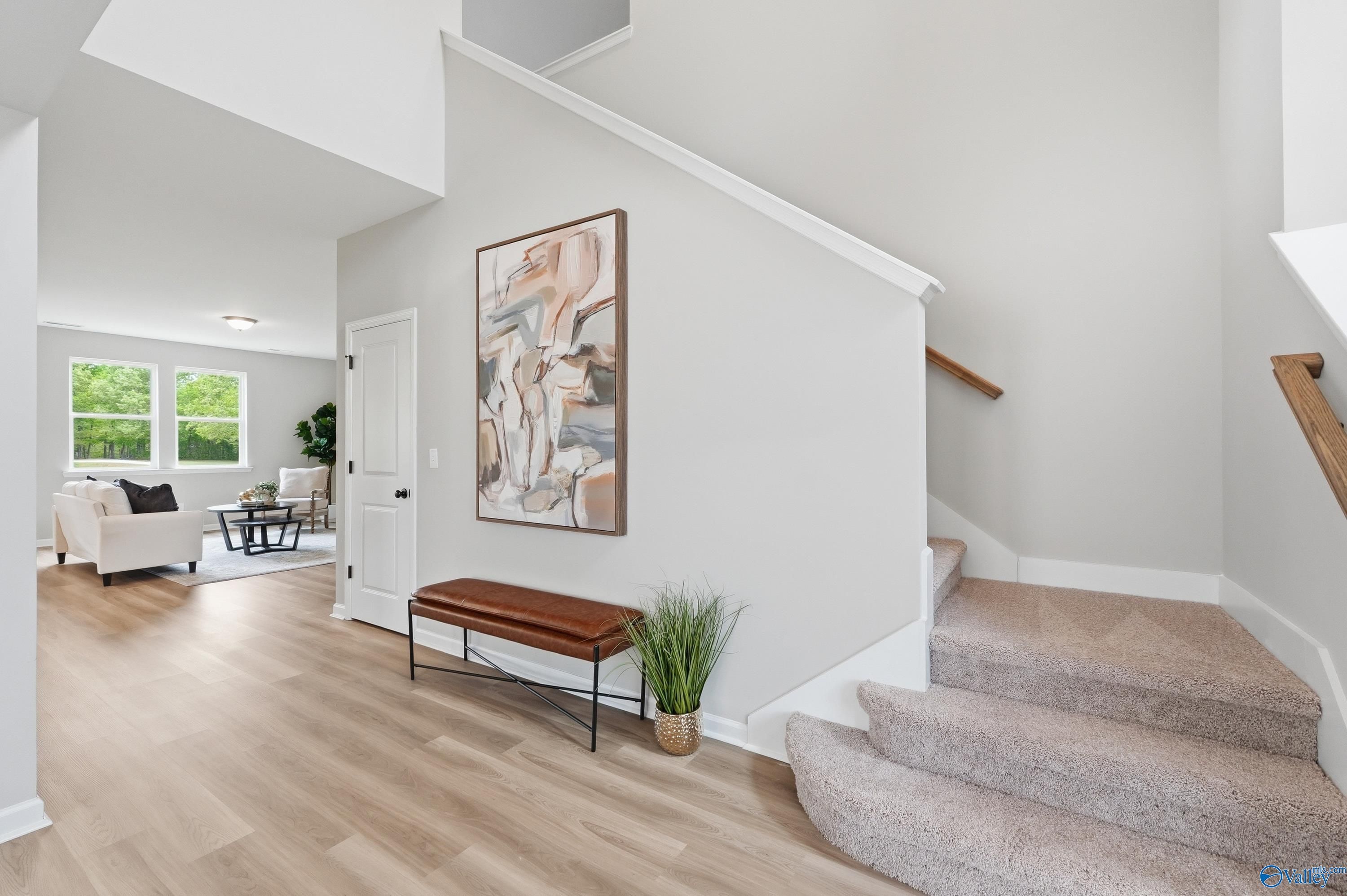 Bright foyer with hardwood floors, white sofa, abstract art, potted plants, and carpeted staircase in Davidson Homes The Dorado, Huntsville