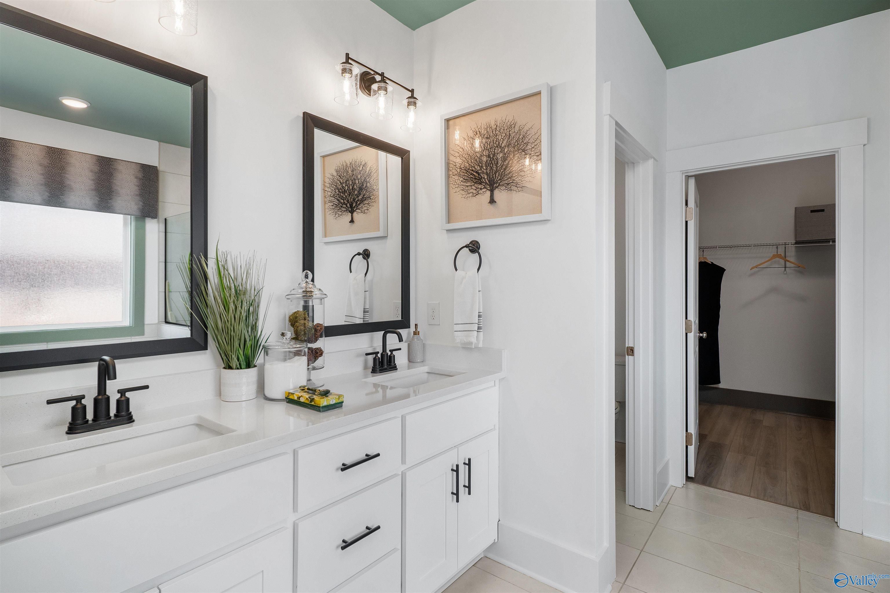 Modern master bathroom featuring double white vanity, black-framed mirrors, green ceiling, and walk-in closet in Davidson Homes The Rockford B, Madison, Alabama