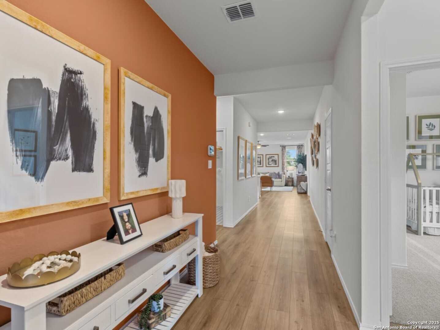 Elegant hallway with orange accent wall, abstract art, console table, and nursery view in Davidson Homes The Daphne E, Elmendorf, Texas