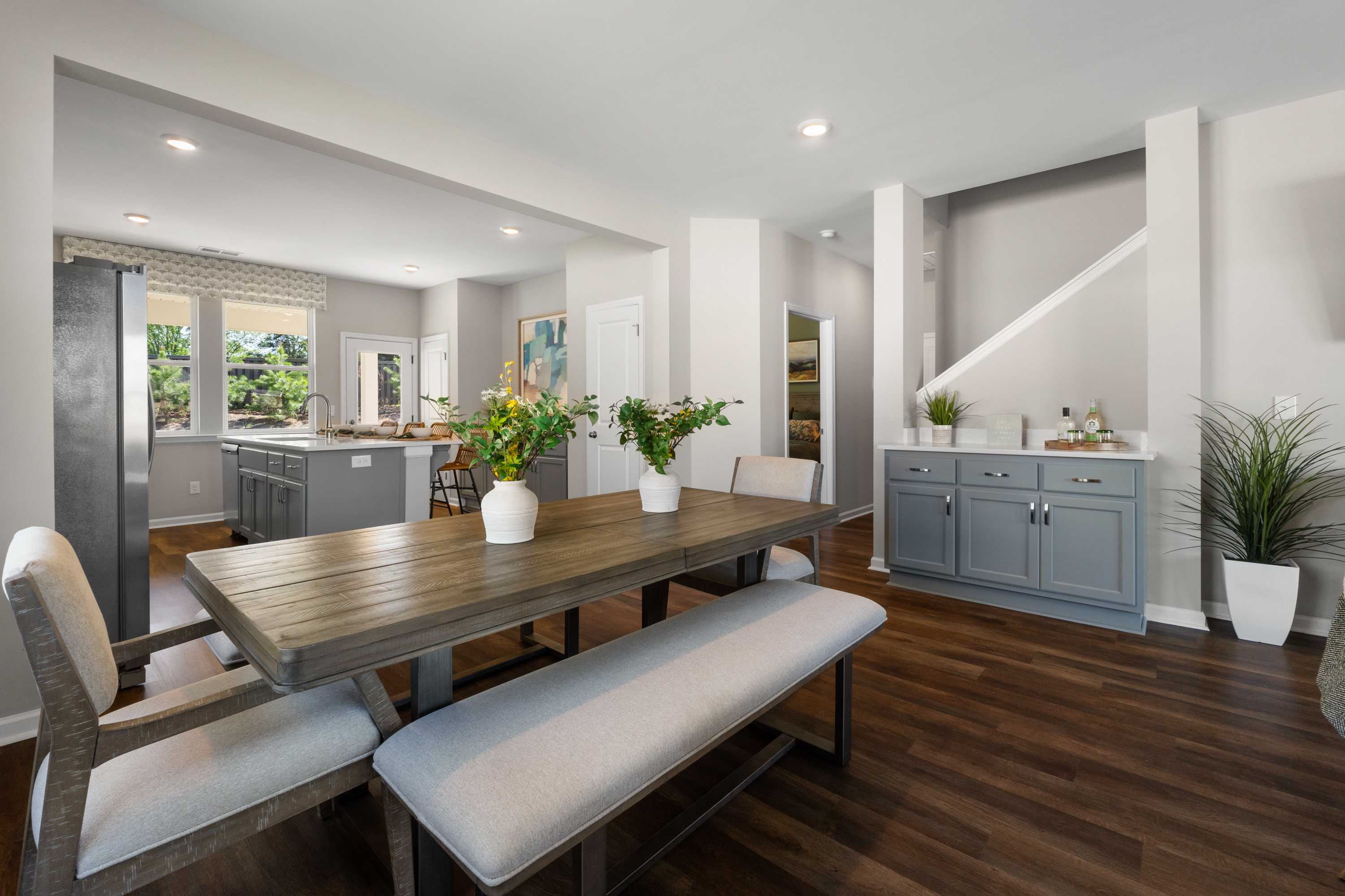 Open-concept dining area at Evergreen Mill in Madison, Alabama with wooden table, benches, gray kitchen cabinets, and potted plants
