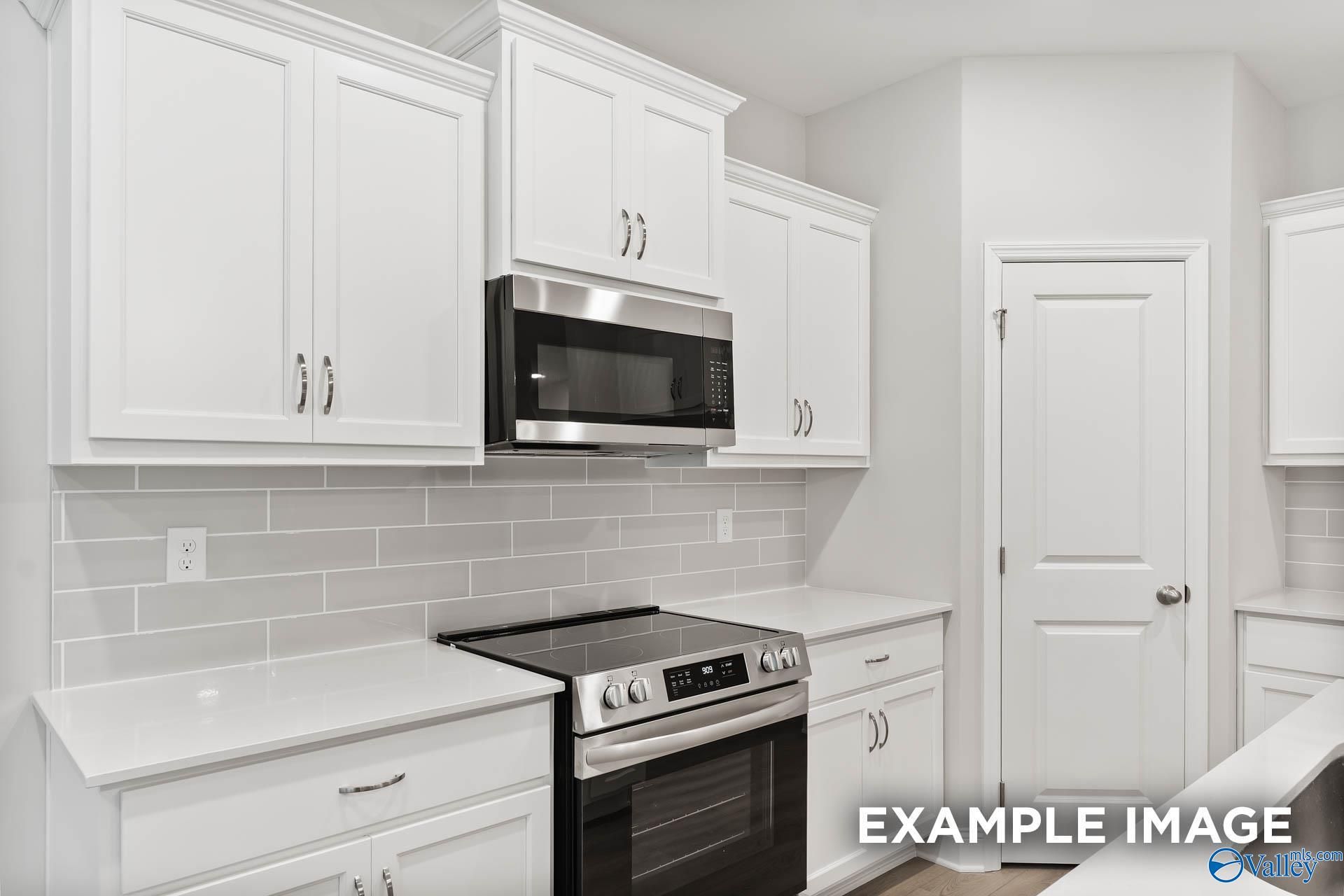Modern white kitchen featuring stainless steel microwave, oven, subway tile backsplash in The Asheville C floor plan, Davidson Homes Huntsville AL