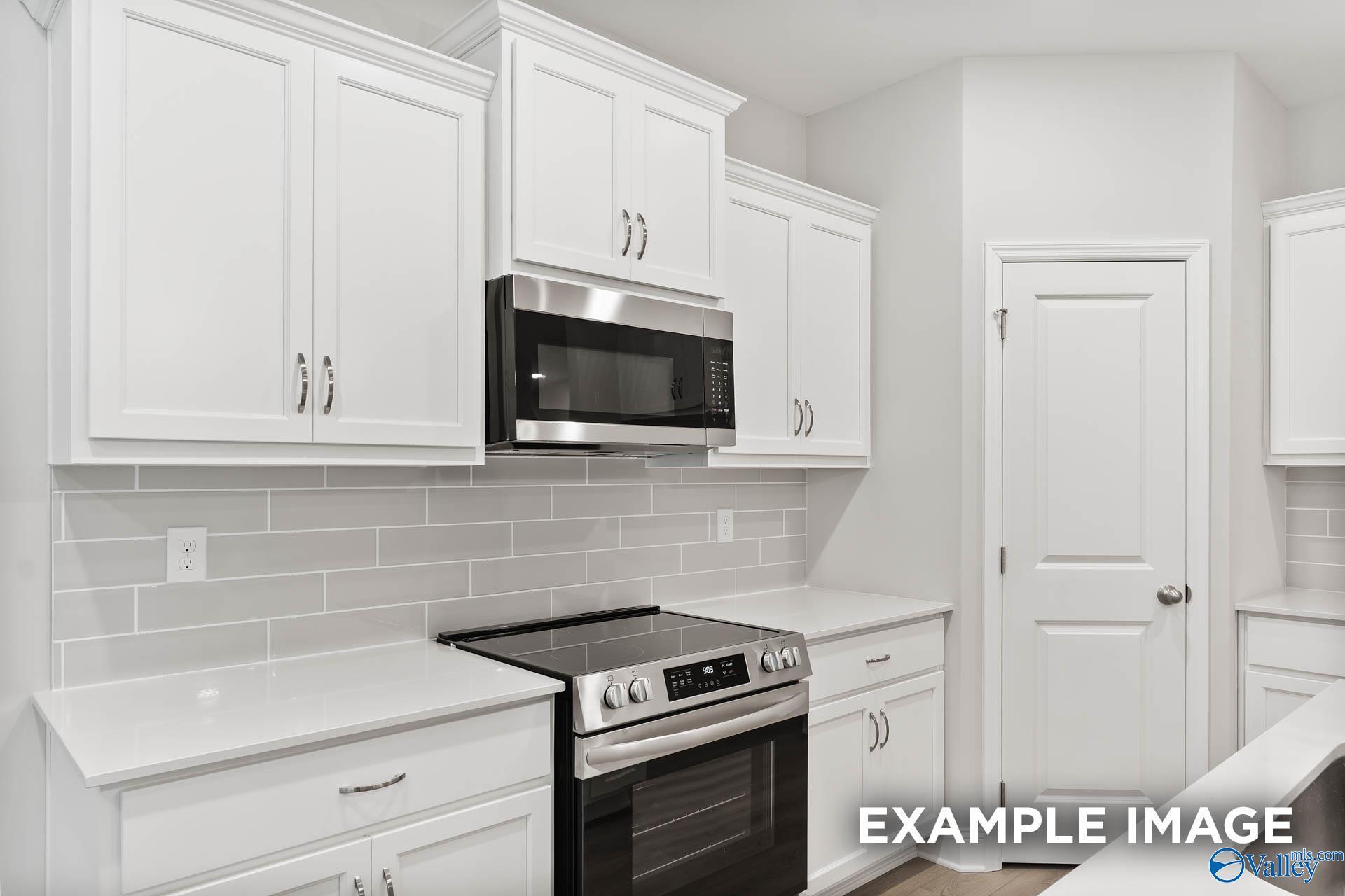Modern white kitchen featuring stainless steel cooktop, oven, and microwave with subway tile backsplash in Davidson Homes The Asheville, Huntsville AL