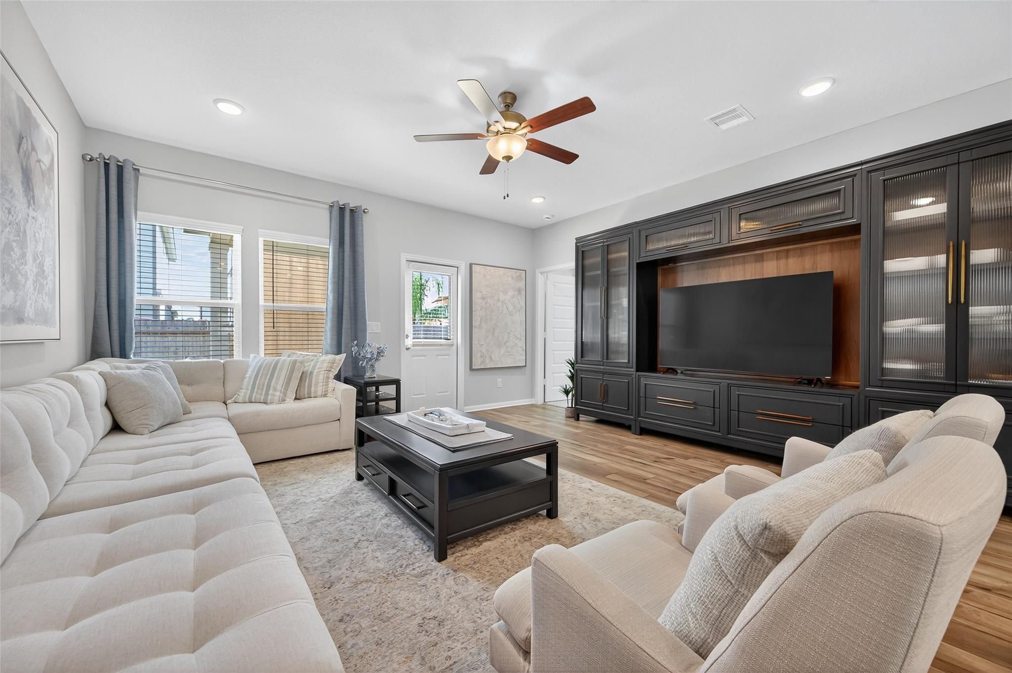 Cozy living room with beige sofas, dark wood TV cabinet, ceiling fan, and neutral decor in Davidson Homes The Brazos E, Magnolia, Texas