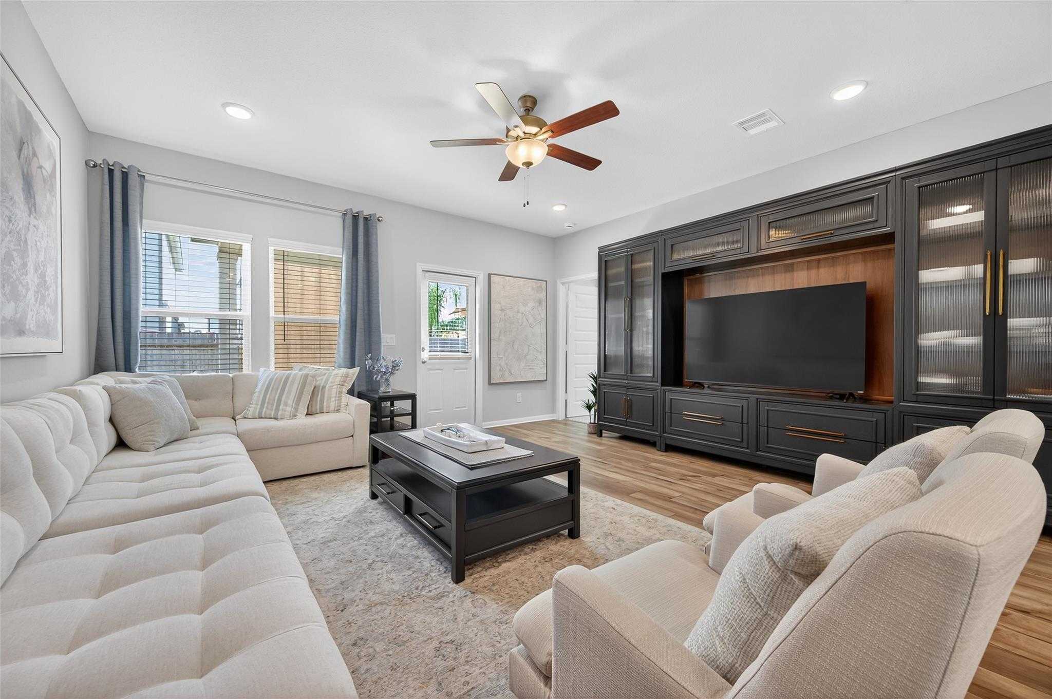 Cozy living room with beige sofas, dark wood TV cabinet, ceiling fan, and neutral decor in Davidson Homes The Brazos E, Magnolia, Texas