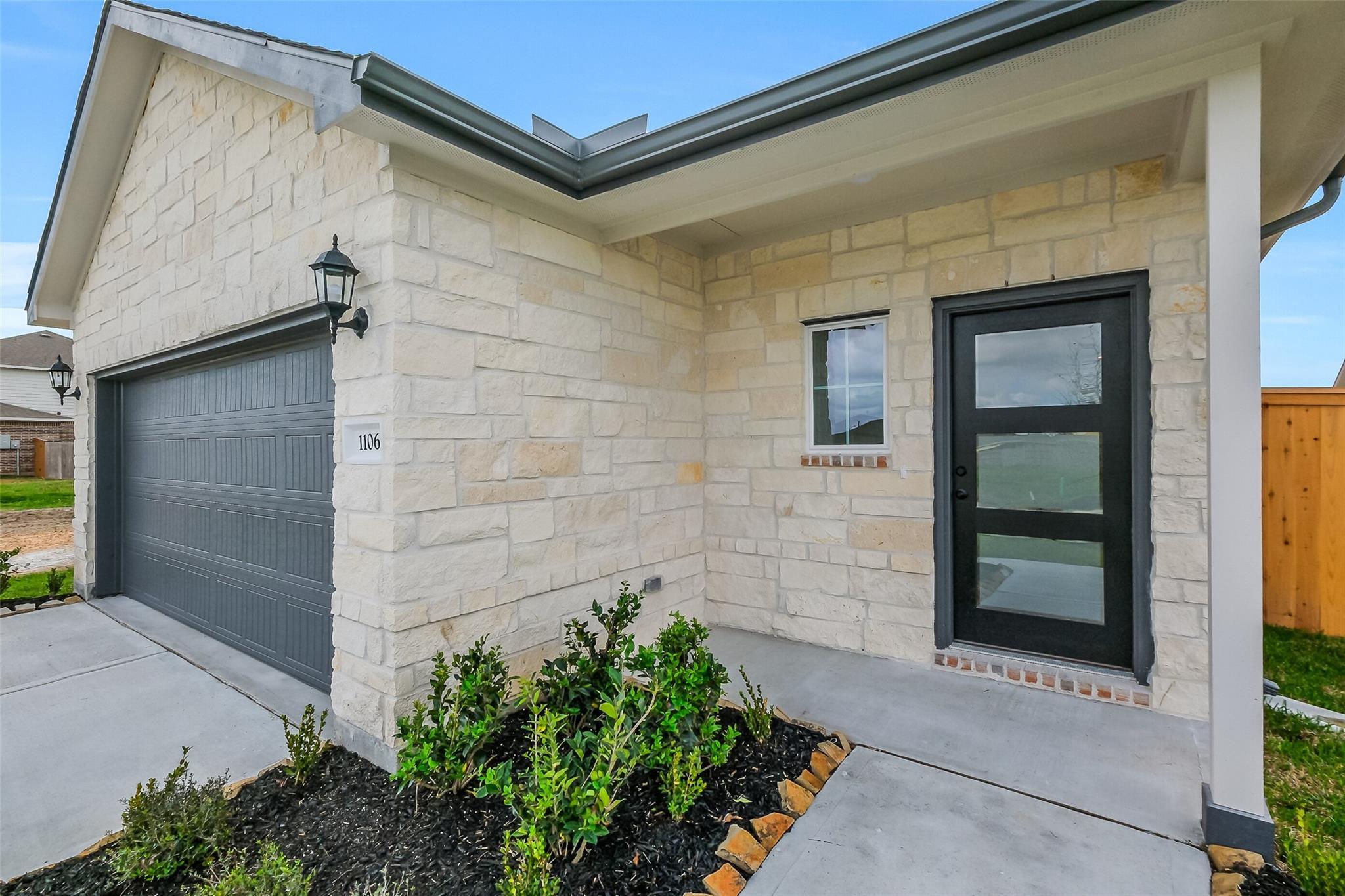 Beige stone facade 2-story home with 2-car garage, black glass entry door, covered porch, and landscaped front in Emberly, Beasley, Texas