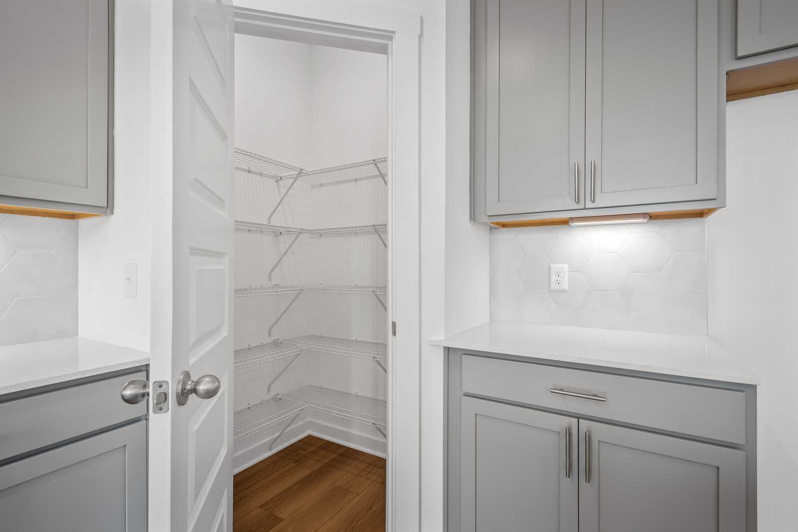 Walk-in pantry with white wire shelving in The Asheville home design, adjacent to gray kitchen cabinets and quartz counter