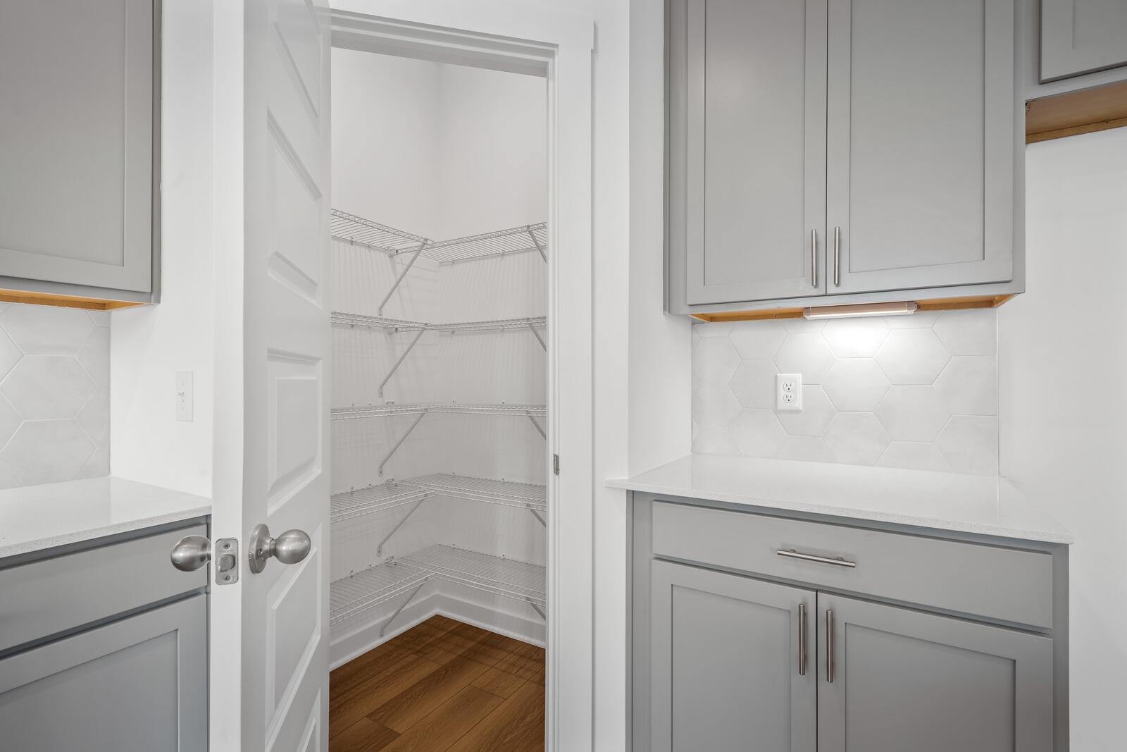 Spacious walk-in pantry open to modern kitchen in The Asheville design with gray shaker cabinets, white quartz counters