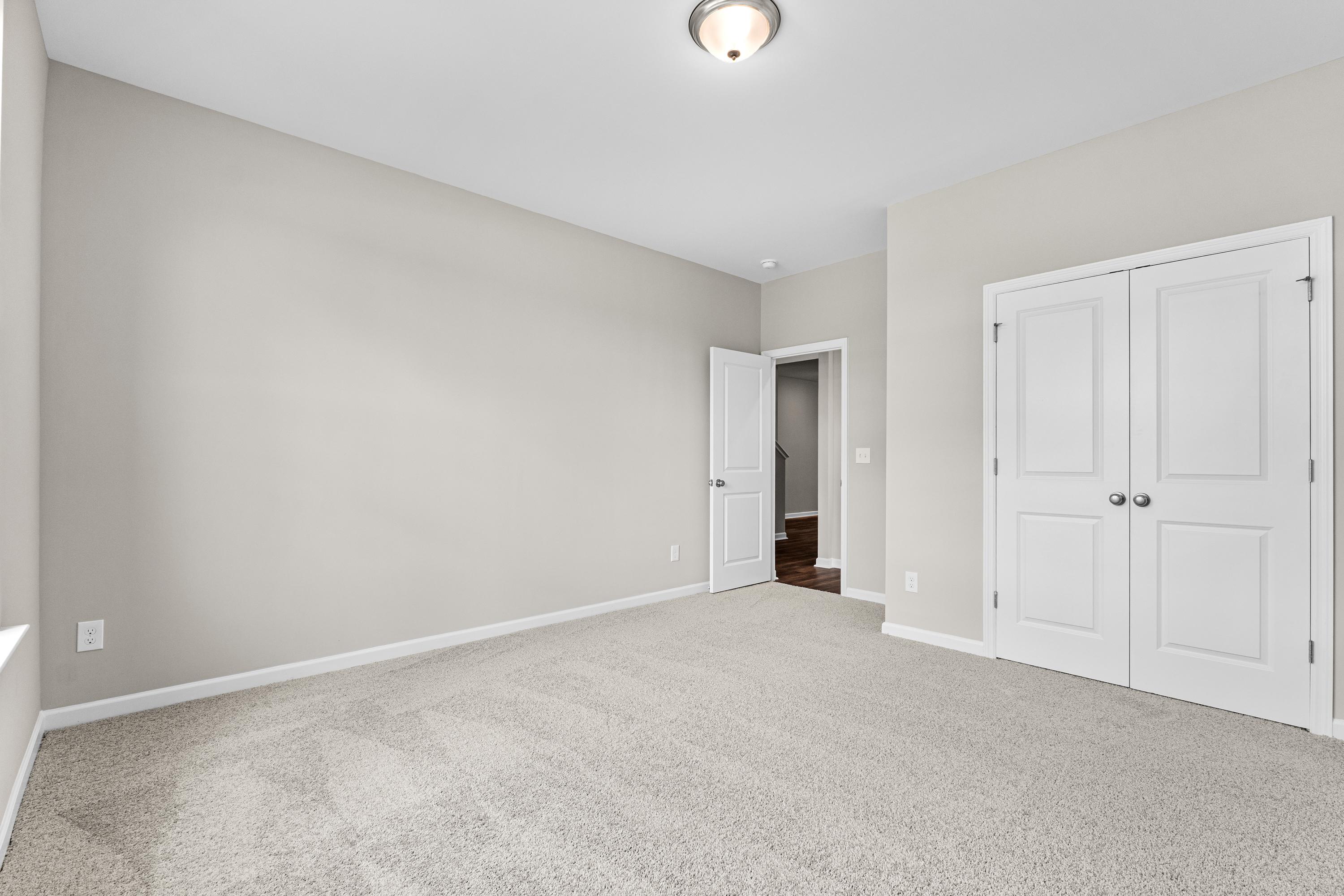Spacious bedroom in The Haven E by Evermore Homes, light gray walls, beige carpet, white double doors, and en-suite access