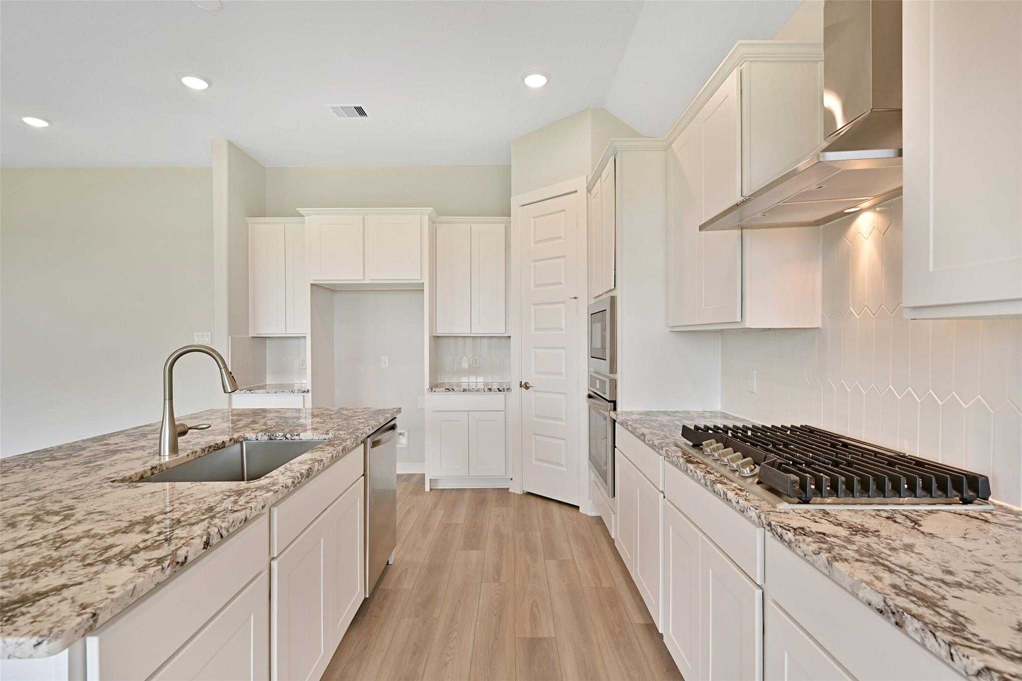Modern white kitchen with granite island, stainless double ovens, gas range, subway backsplash in Davidson Homes The Edward A, Lago Mar, Texas City