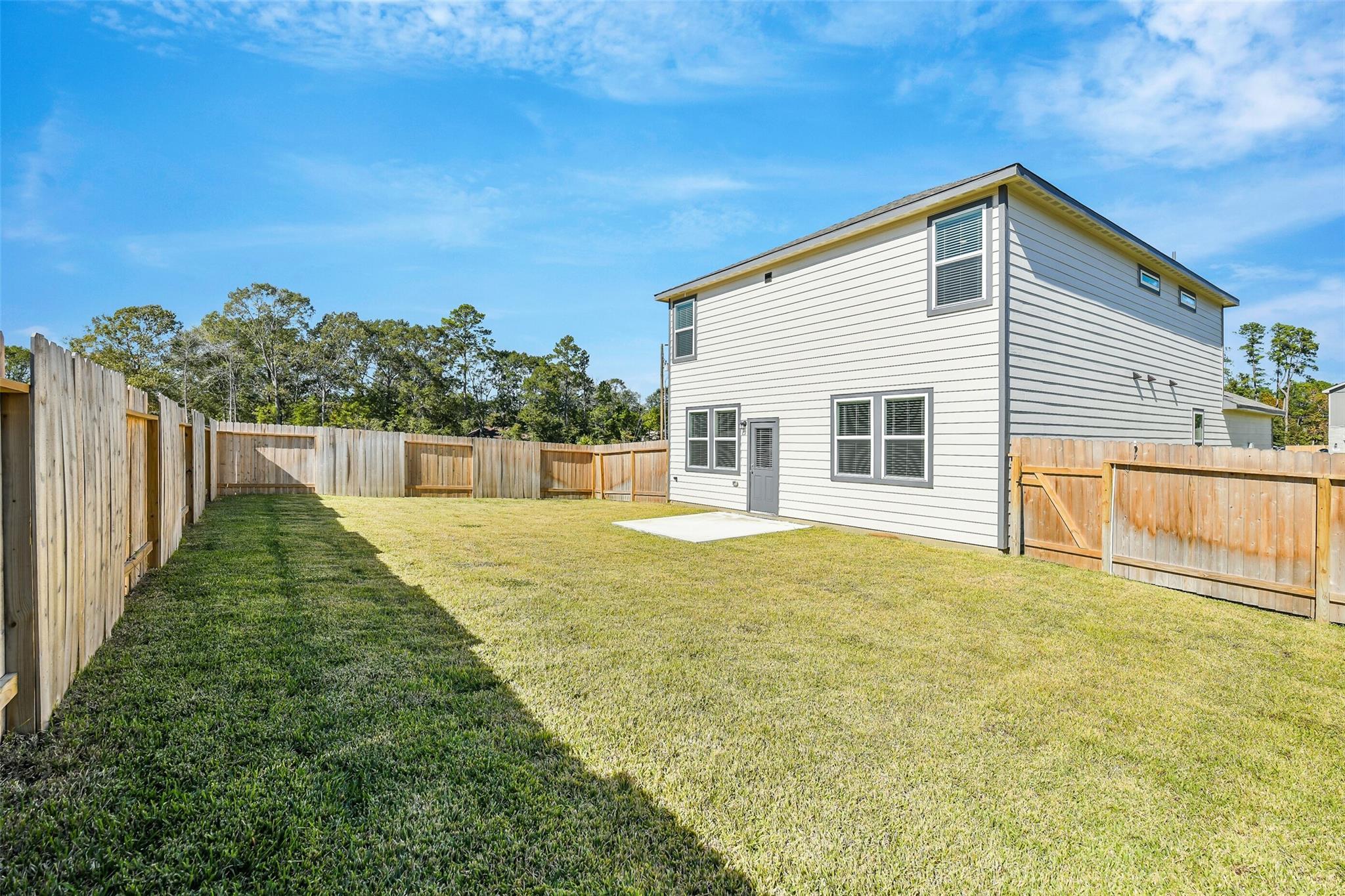 Two-story San Marcos E home exterior with fenced grassy backyard and trees in Liberty Estates, Cleveland, Texas