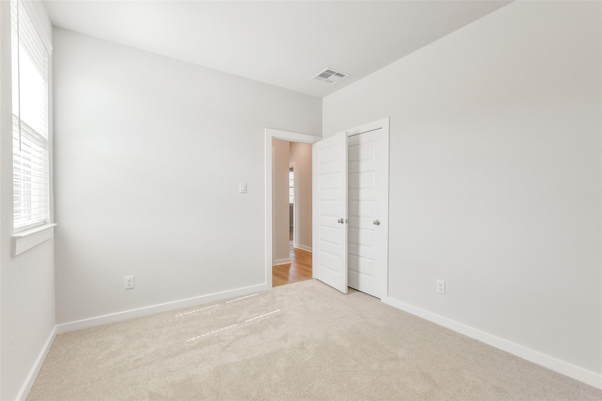 Bright secondary bedroom with white walls, beige carpet, window blinds, and open door to hallway in Davidson Homes The Colorado F, Cleveland, Texas