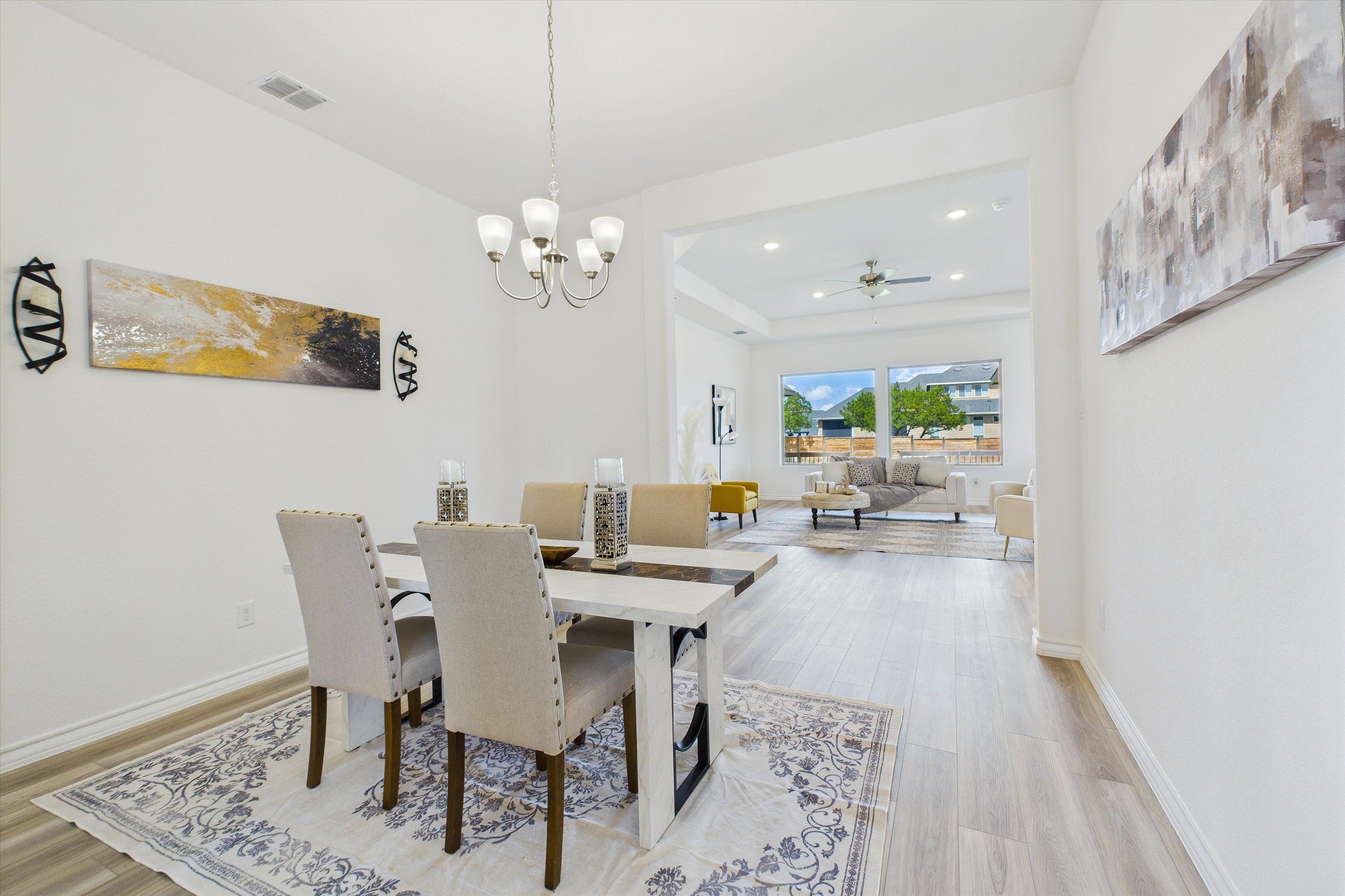 Elegant dining room with white chandelier, farmhouse table, tufted chairs, and blue rug opening to living area in Davidson Homes Summerlin C, Castroville, Texas