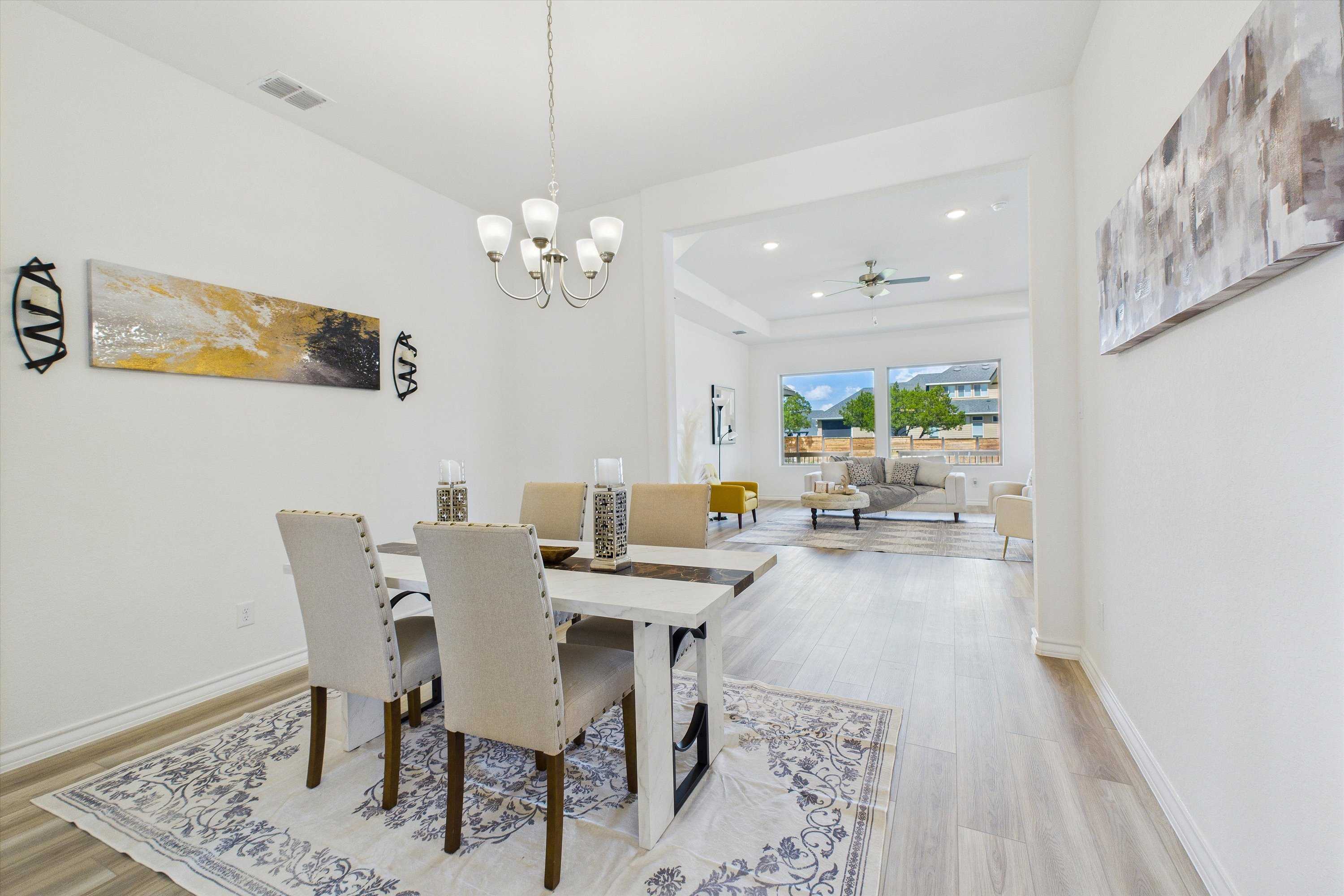 Elegant dining room with white chandelier, farmhouse table, tufted chairs, and blue rug opening to living area in Davidson Homes Summerlin C, Castroville, Texas