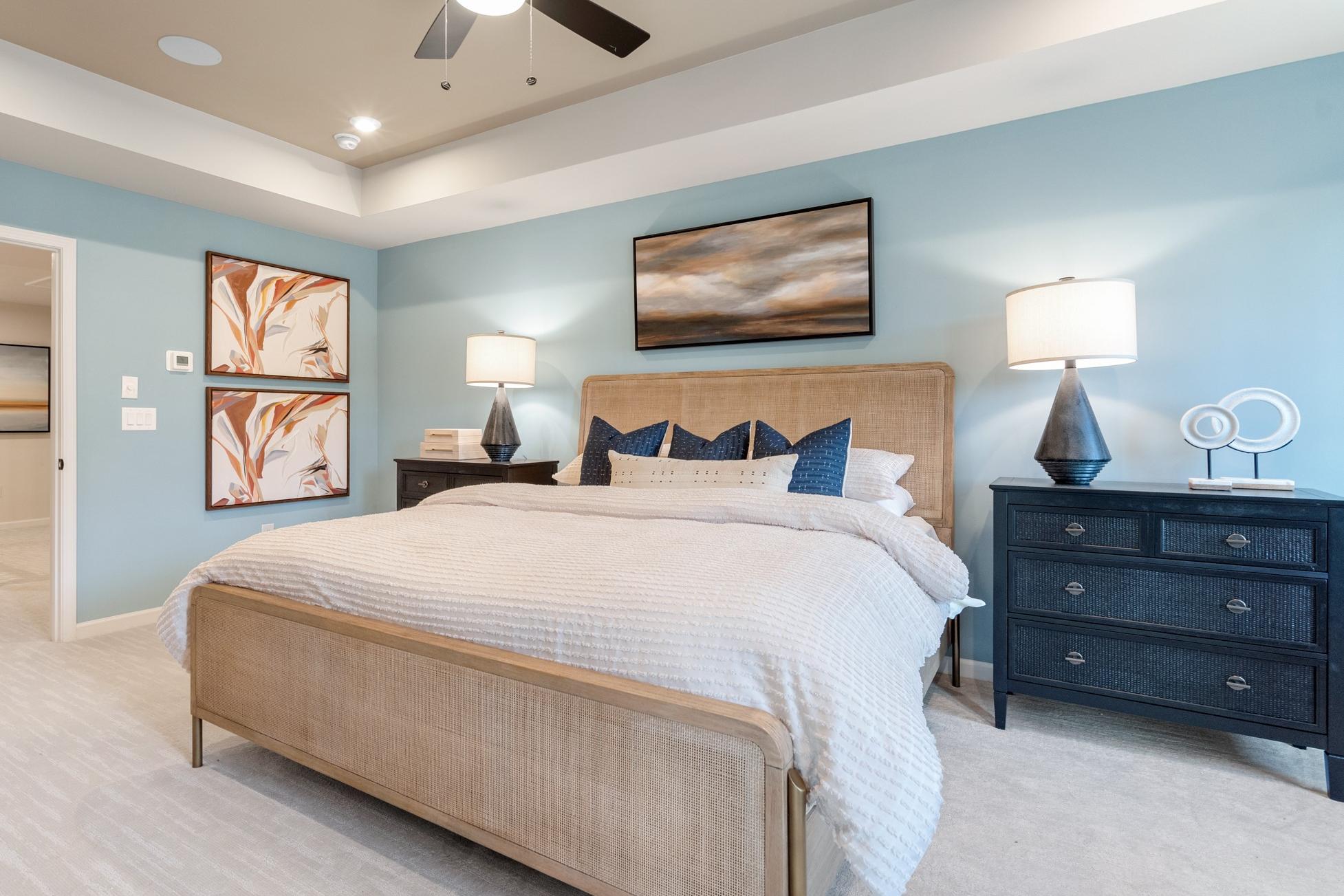 Master bedroom at The Village at Shallowford in Kennesaw Georgia by Davidson Homes with light blue walls, king bed, ceiling fan and abstract art