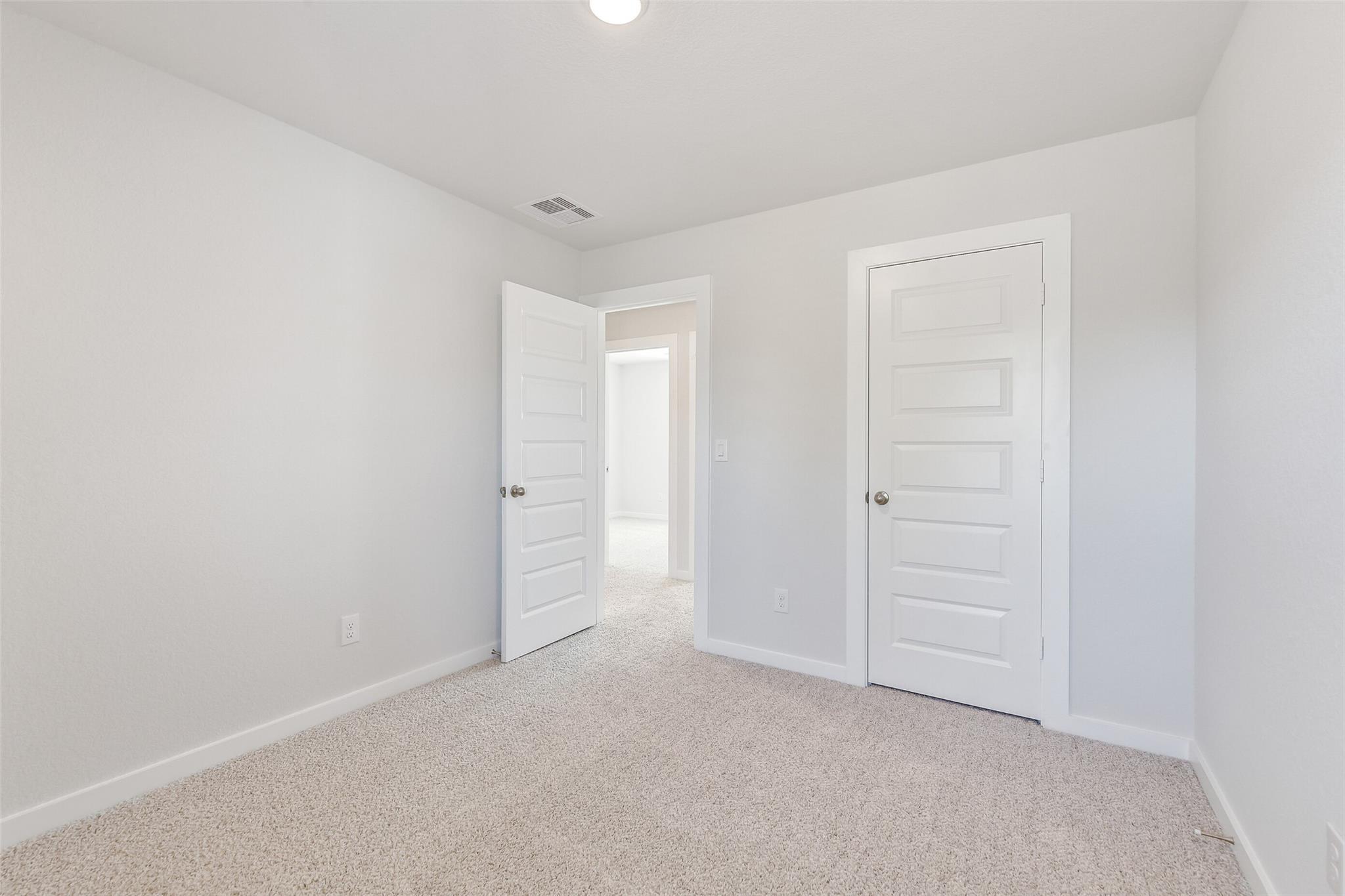Bright secondary bedroom with white paneled doors, beige carpet, and neutral walls in Davidson Homes The Blanco E, Magnolia TX