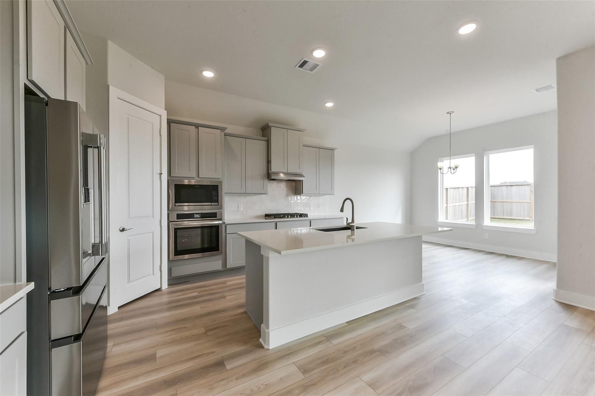 Modern open-concept kitchen with white shaker cabinets, stainless steel appliances, and quartz island in Davidson Homes The Edward A, Texas City