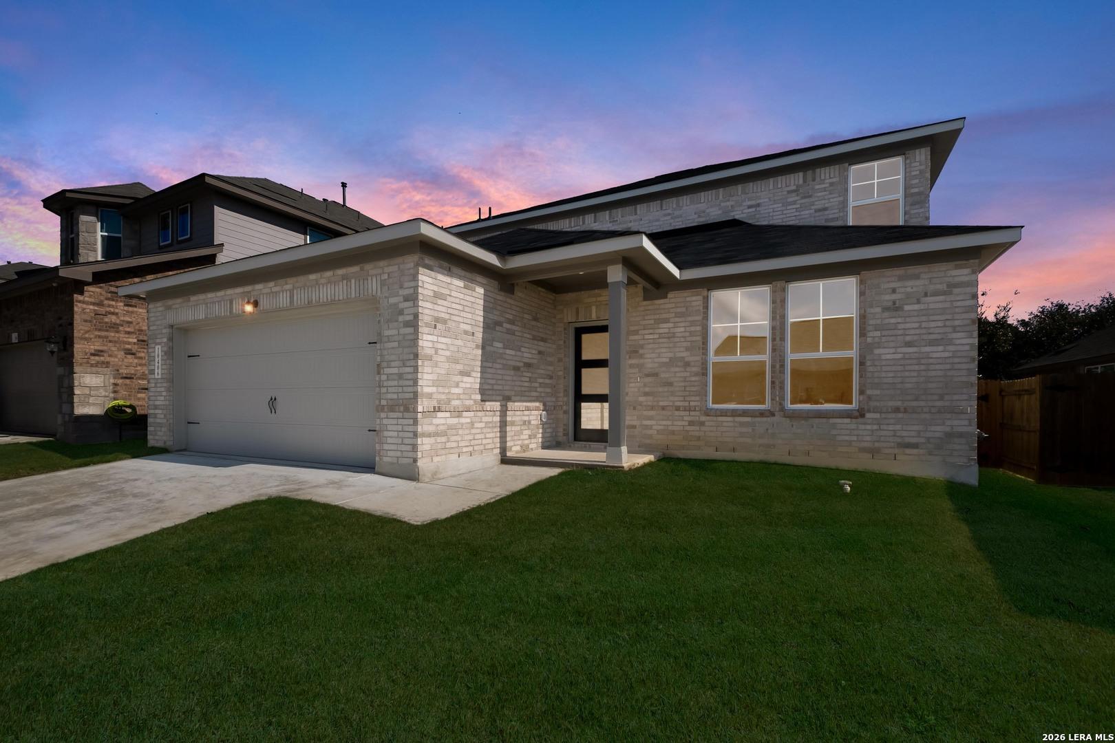 Modern 2-story brick home with 2-car garage, large windows, driveway, and green lawn at sunset in Bricewood, San Antonio - Davidson Homes Douglas E