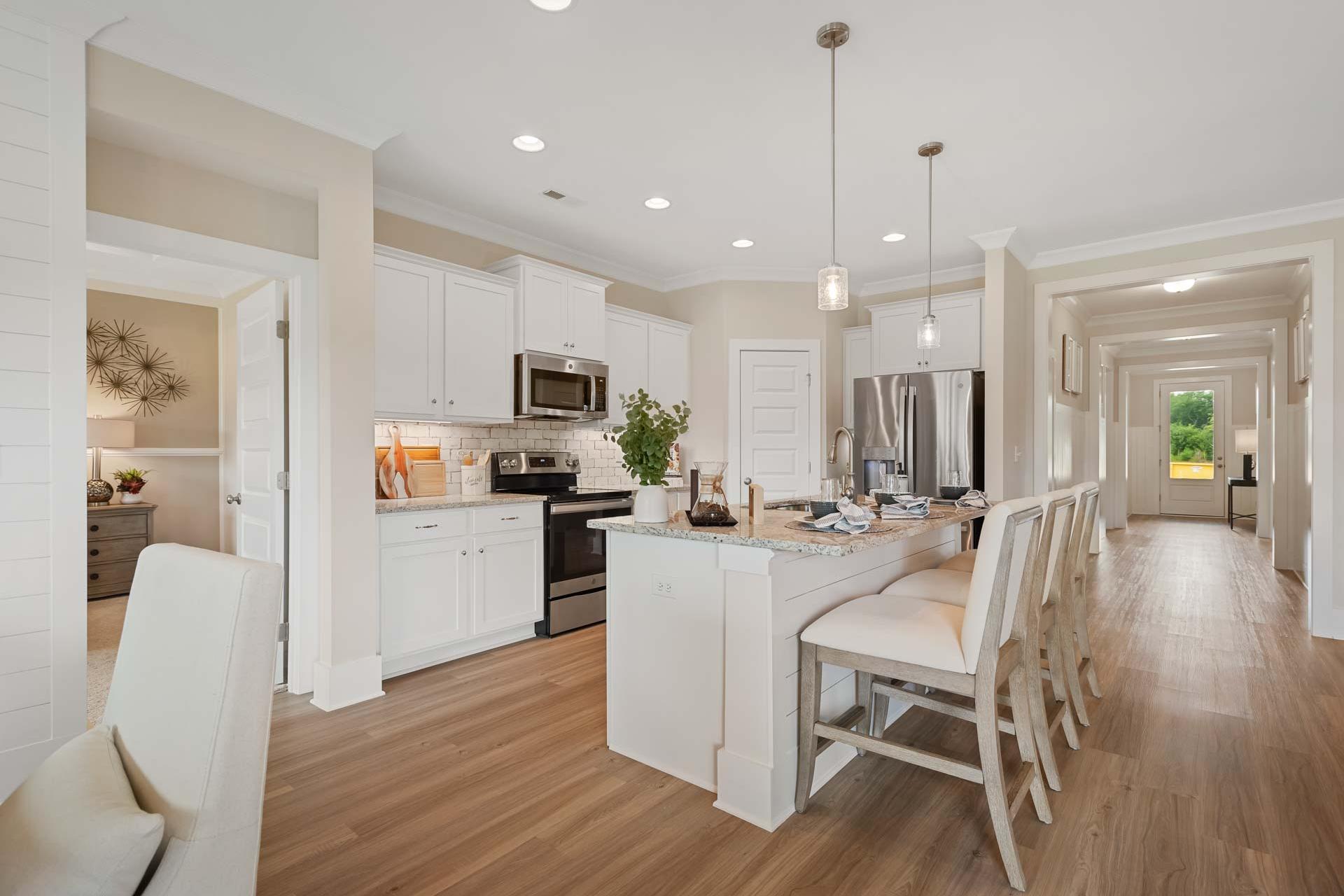 Spacious white kitchen with large island bar seating, stainless appliances, and hardwood floors at Flint Meadows in New Market, Alabama