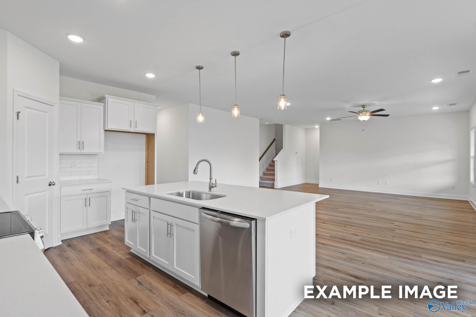 Modern white kitchen island with sink, dishwasher, and pendant lights opens to living area with ceiling fan in Davidson Homes The Rockford B, Athens AL