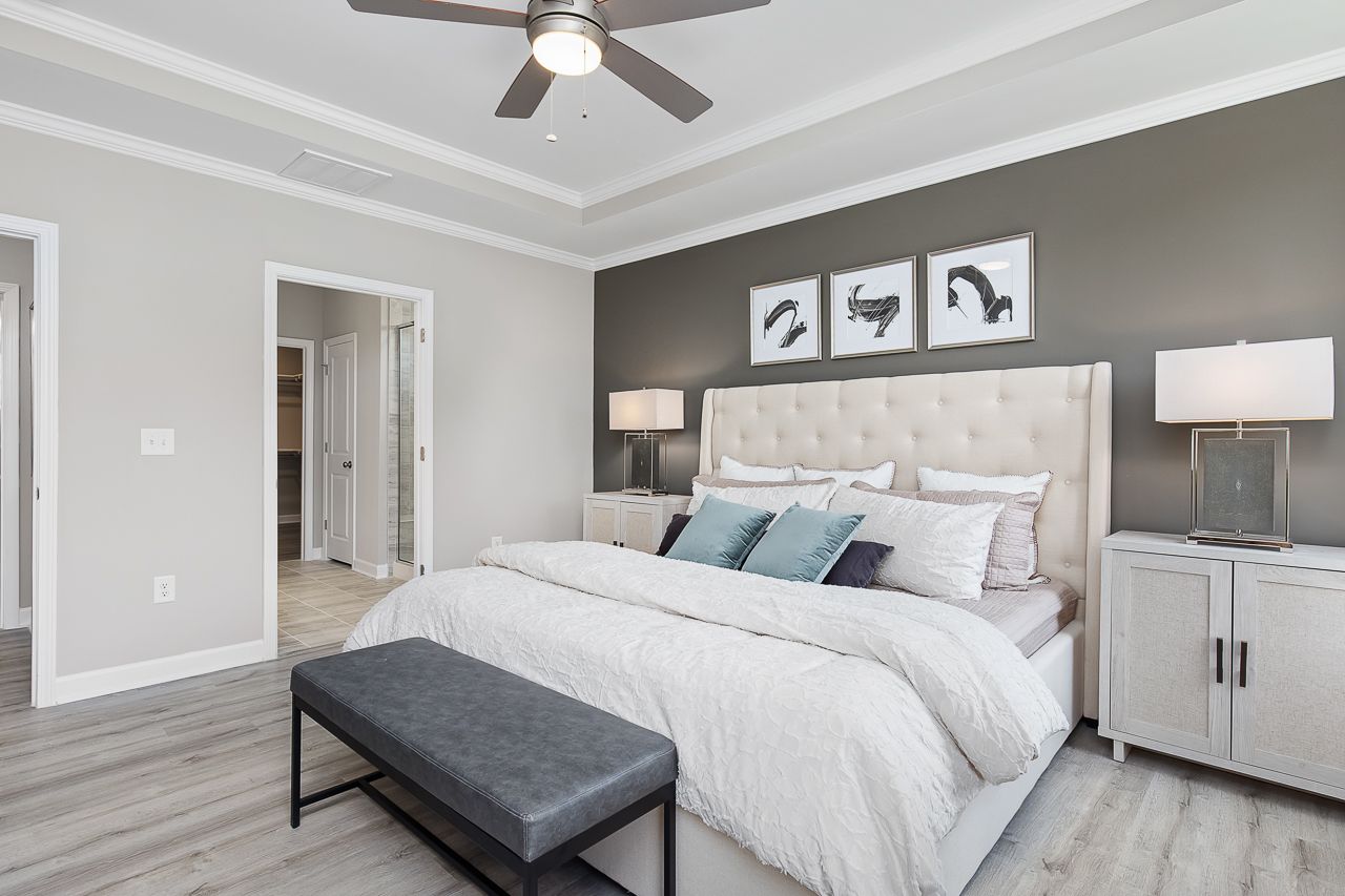 Spacious primary bedroom at Woodland Crossing in Zebulon, NC featuring a tufted headboard, tray ceiling, and modern decor.