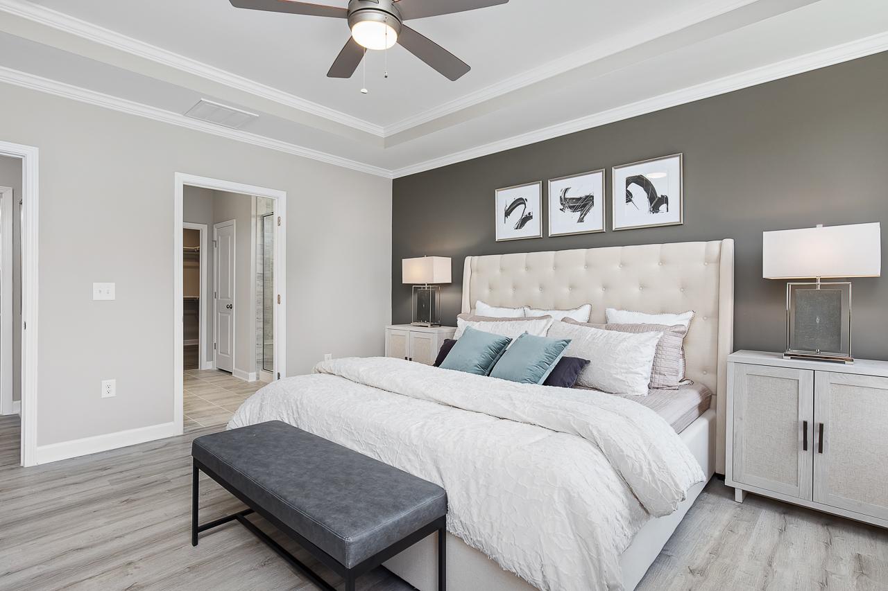 Spacious primary bedroom at Woodland Crossing in Zebulon, NC featuring a tufted headboard, tray ceiling, and modern decor.