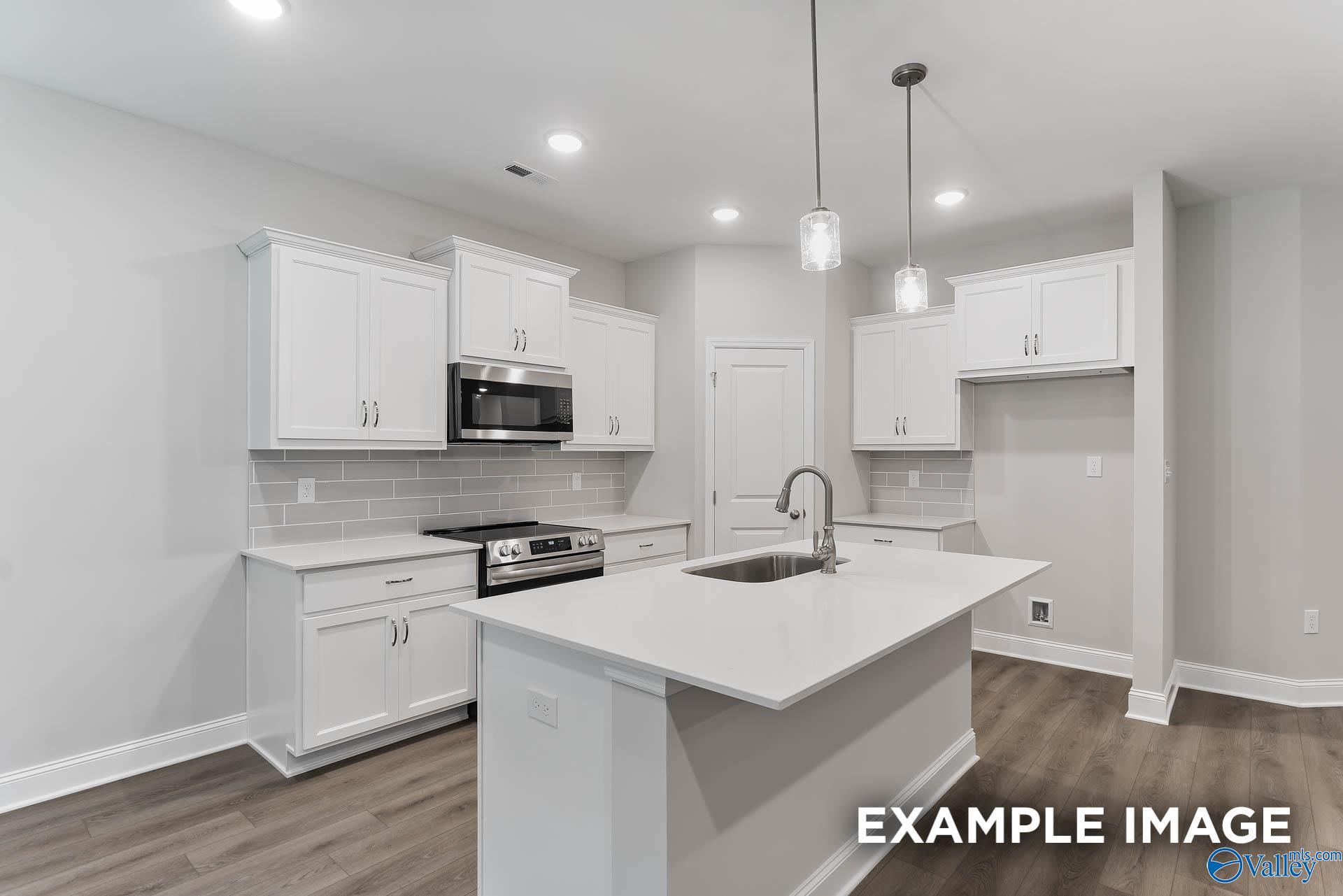 Modern white kitchen with large island, stainless steel appliances, subway tile backsplash in Davidson Homes The Asheville, Huntsville AL