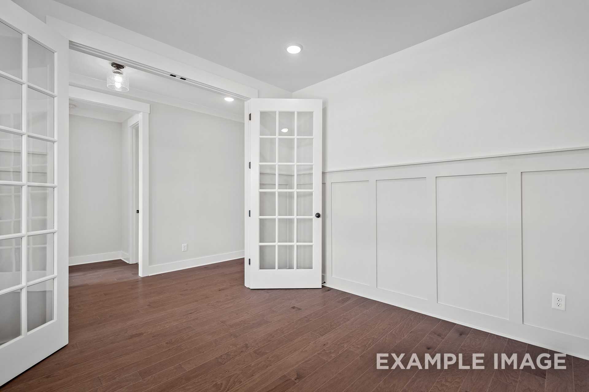 Bright interior of The Hathaway home design with open white French doors, wainscoting, and hardwood floors