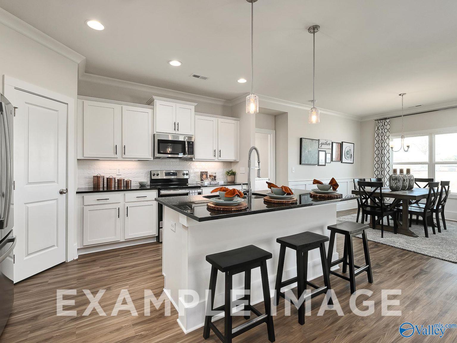 Modern open-concept kitchen with white cabinets, black granite island, stainless appliances, and dining nook in The Everett B, Toney, AL